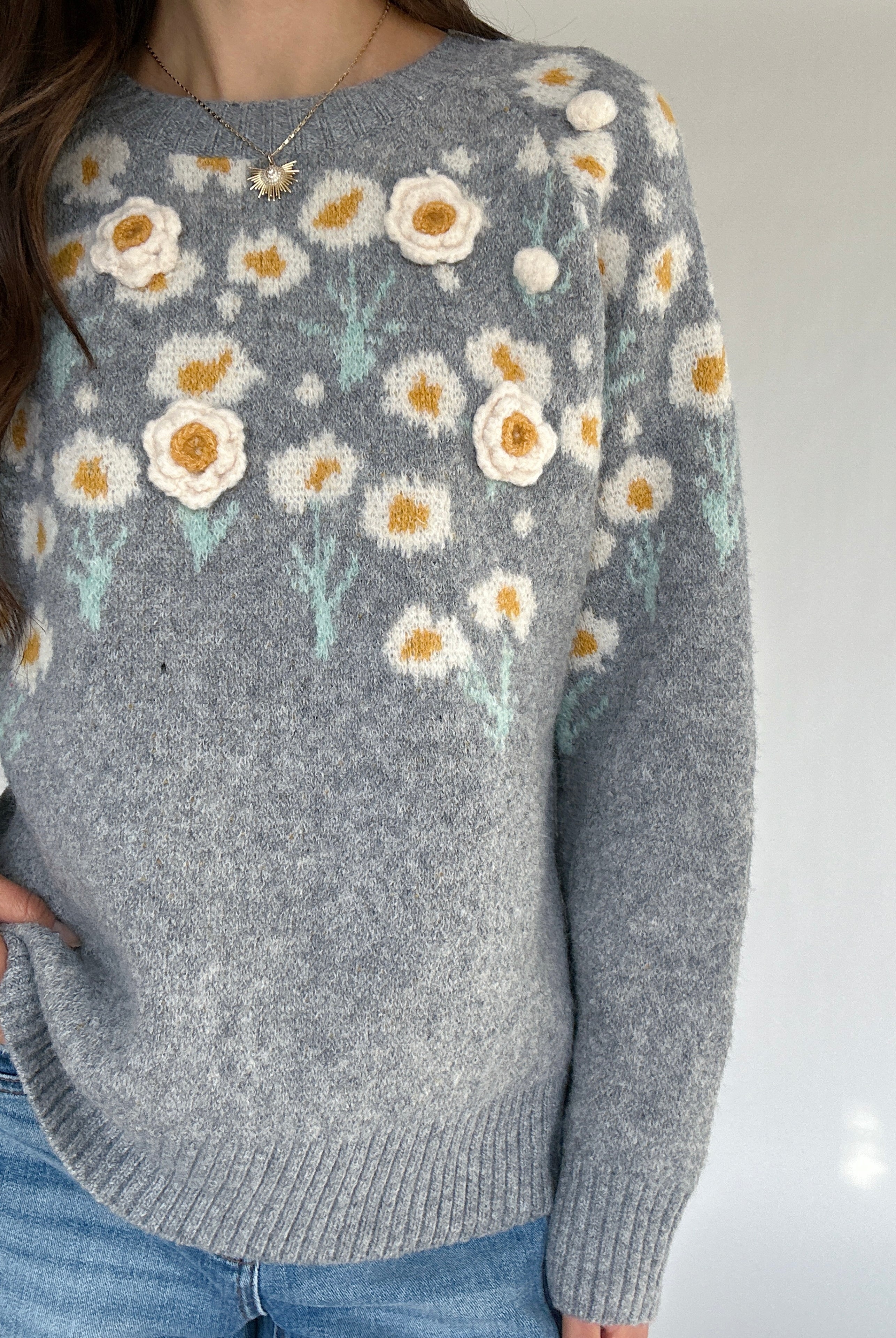 Gray sweater with floral patterns worn by a person on a plain background