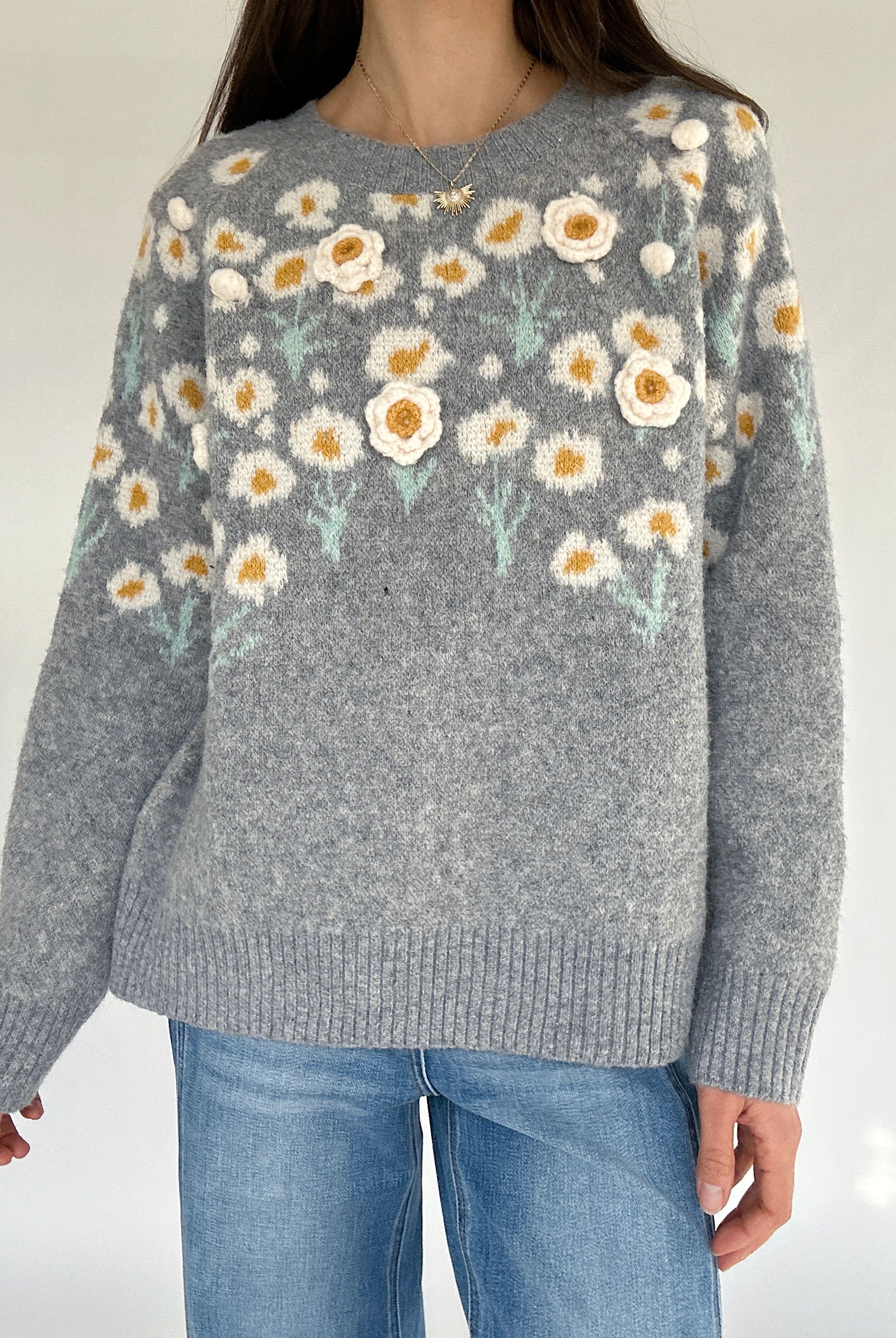 Gray sweater with floral pattern worn by a person against a plain background
