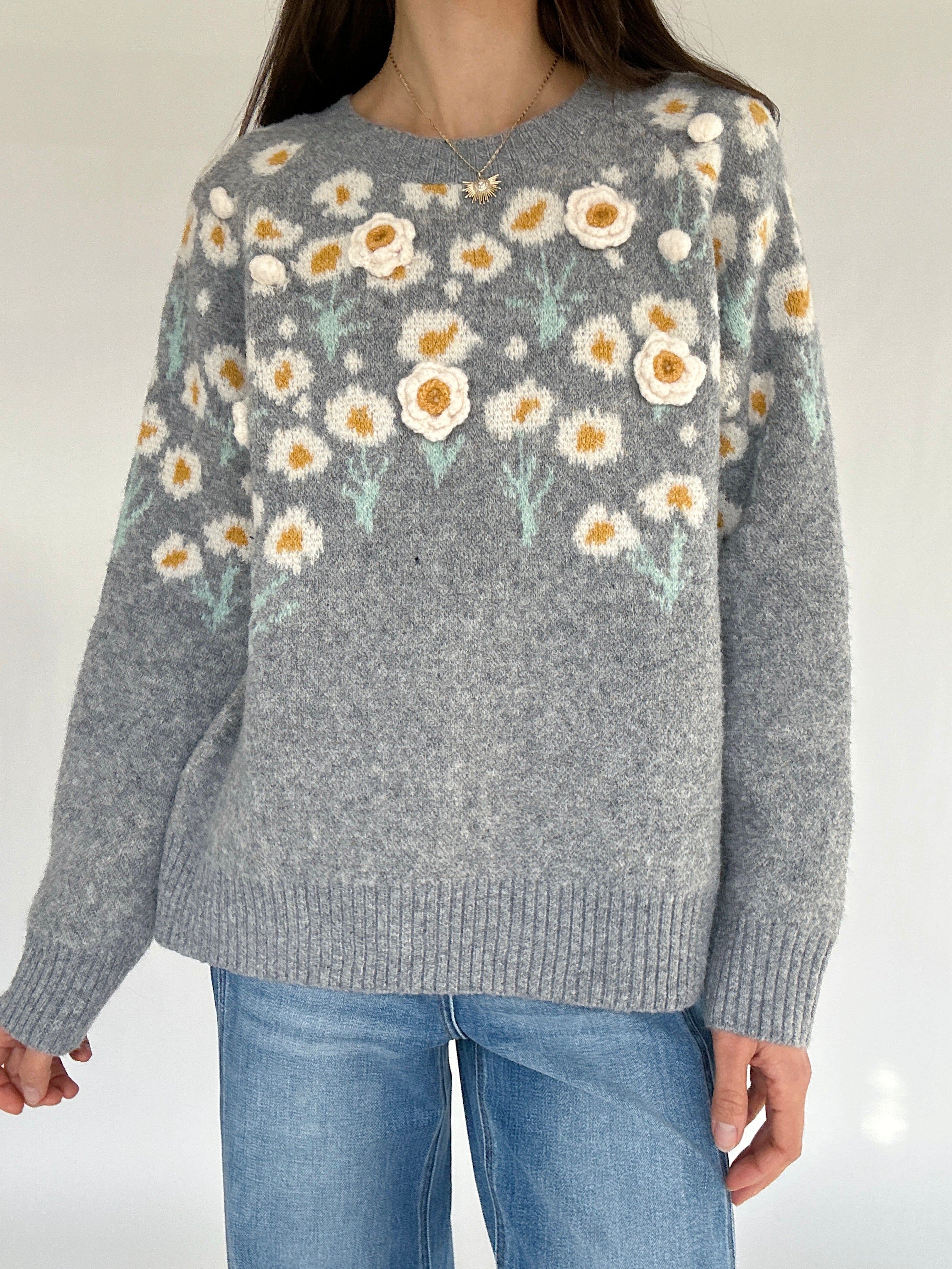 Gray sweater with floral pattern worn by a person against a plain background