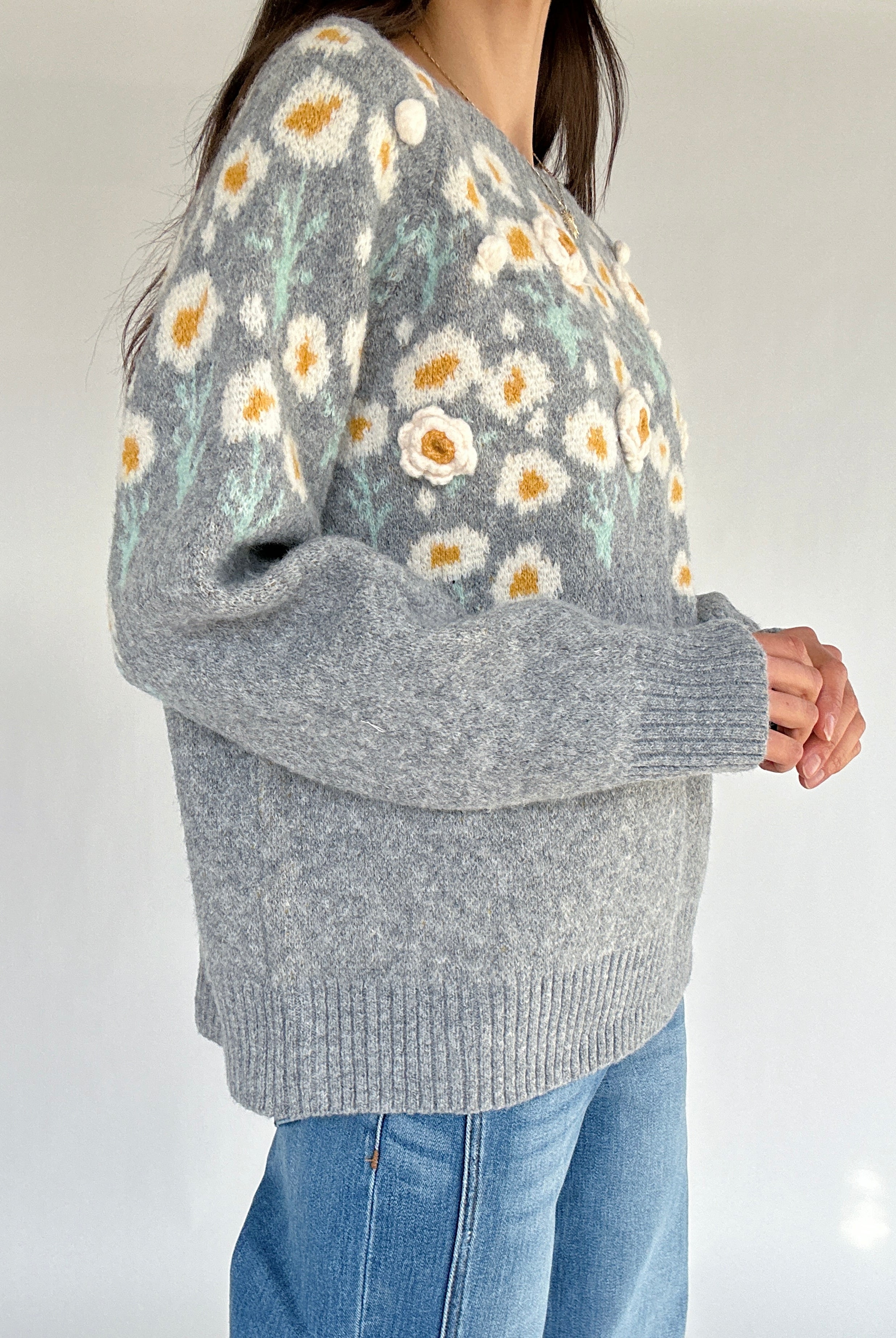 Gray sweater with floral pattern worn by a person on a plain background