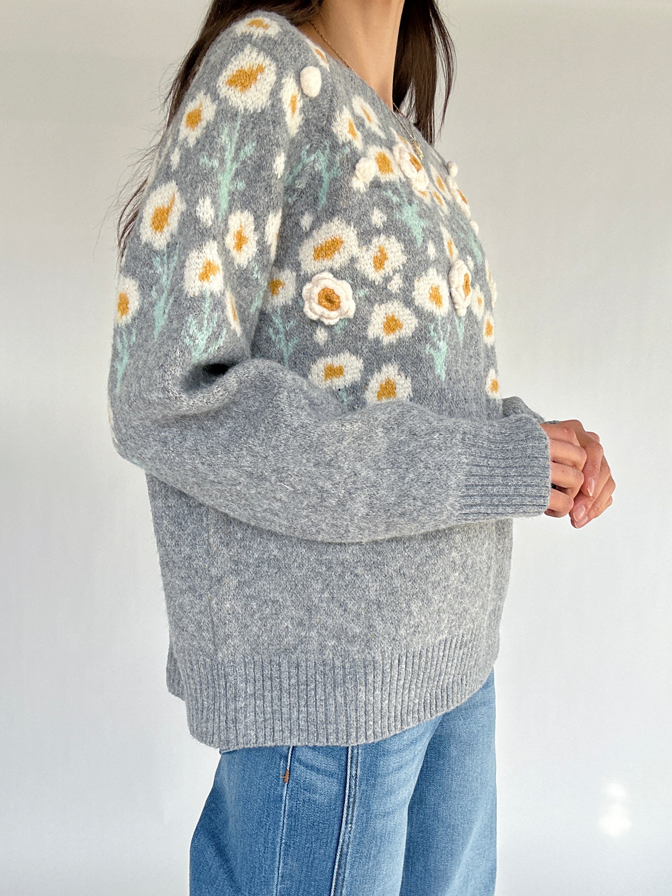 Gray sweater with floral pattern worn by a person on a plain background