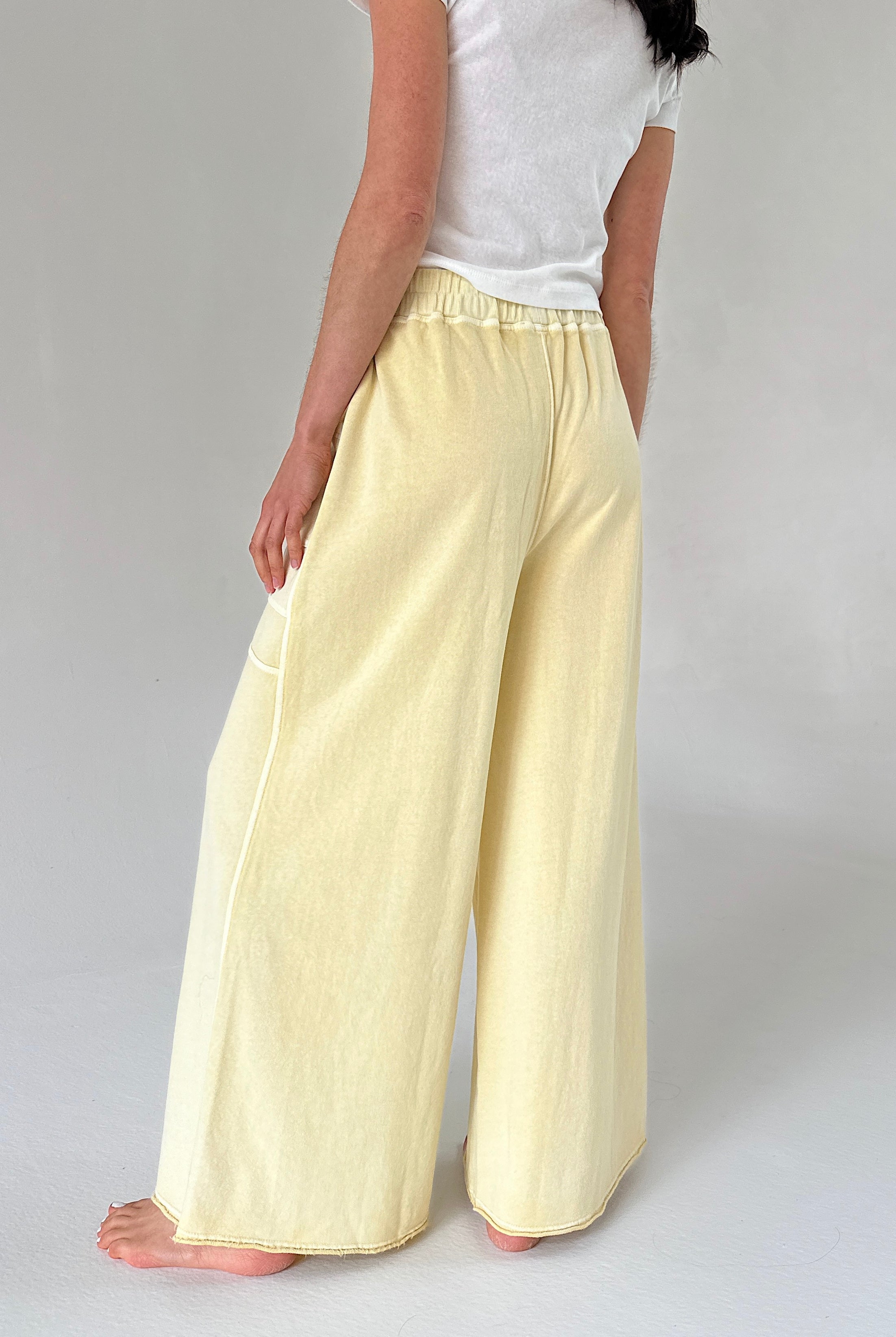 Person wearing light yellow pants and a white top on a plain background