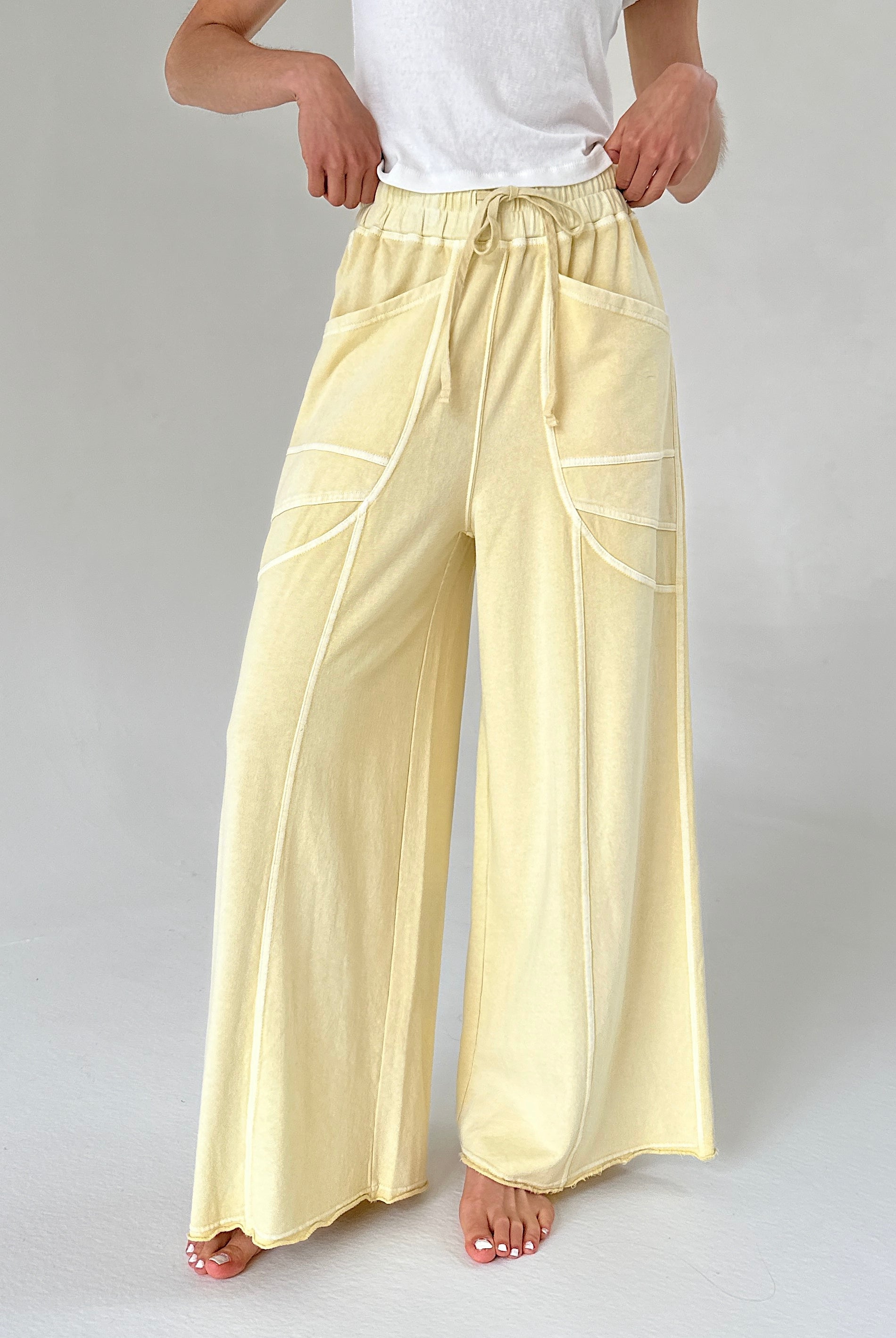 Person wearing light yellow pants with white lines on a plain background