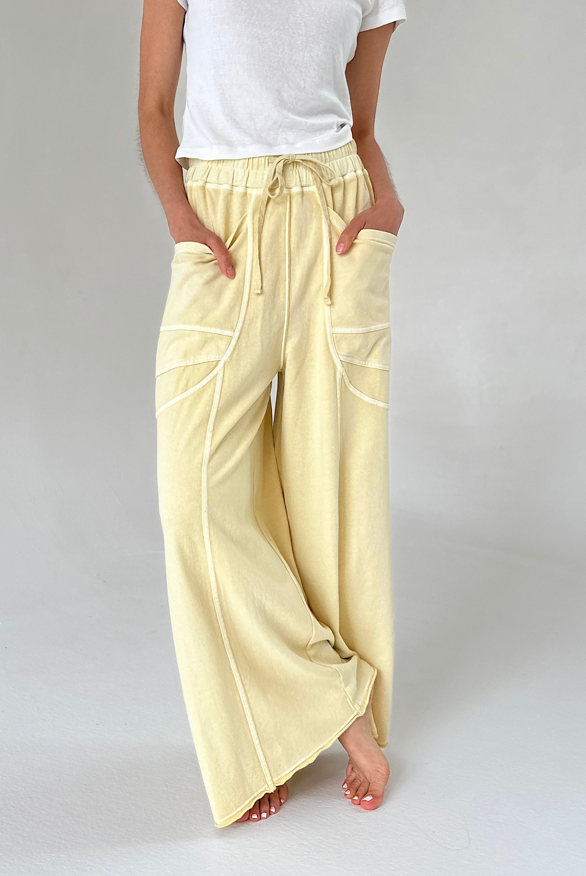 Person wearing light yellow wide-leg pants and a white top on a plain background