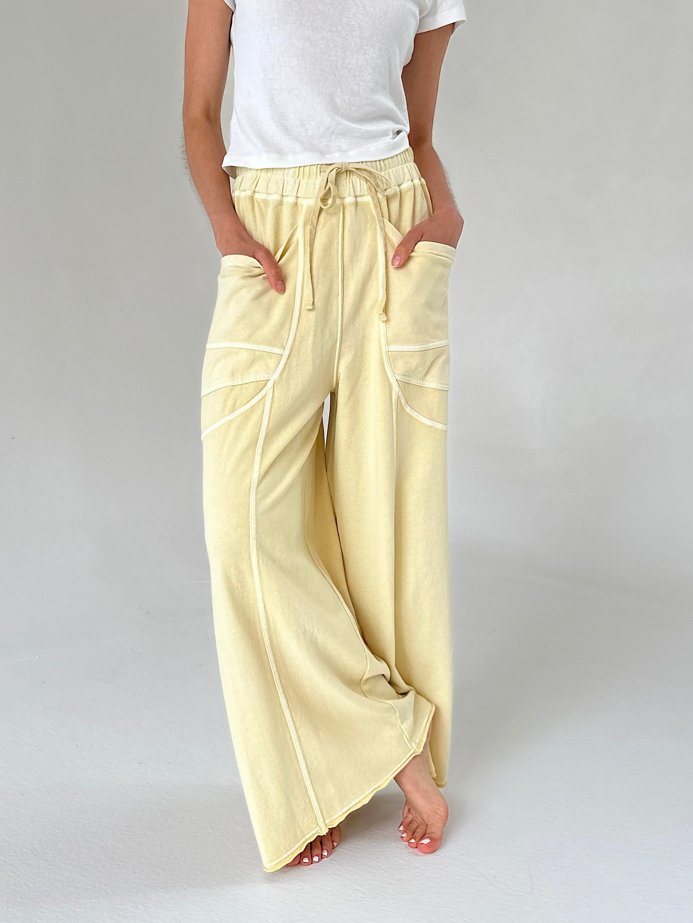 Person wearing light yellow wide-leg pants and a white top on a plain background