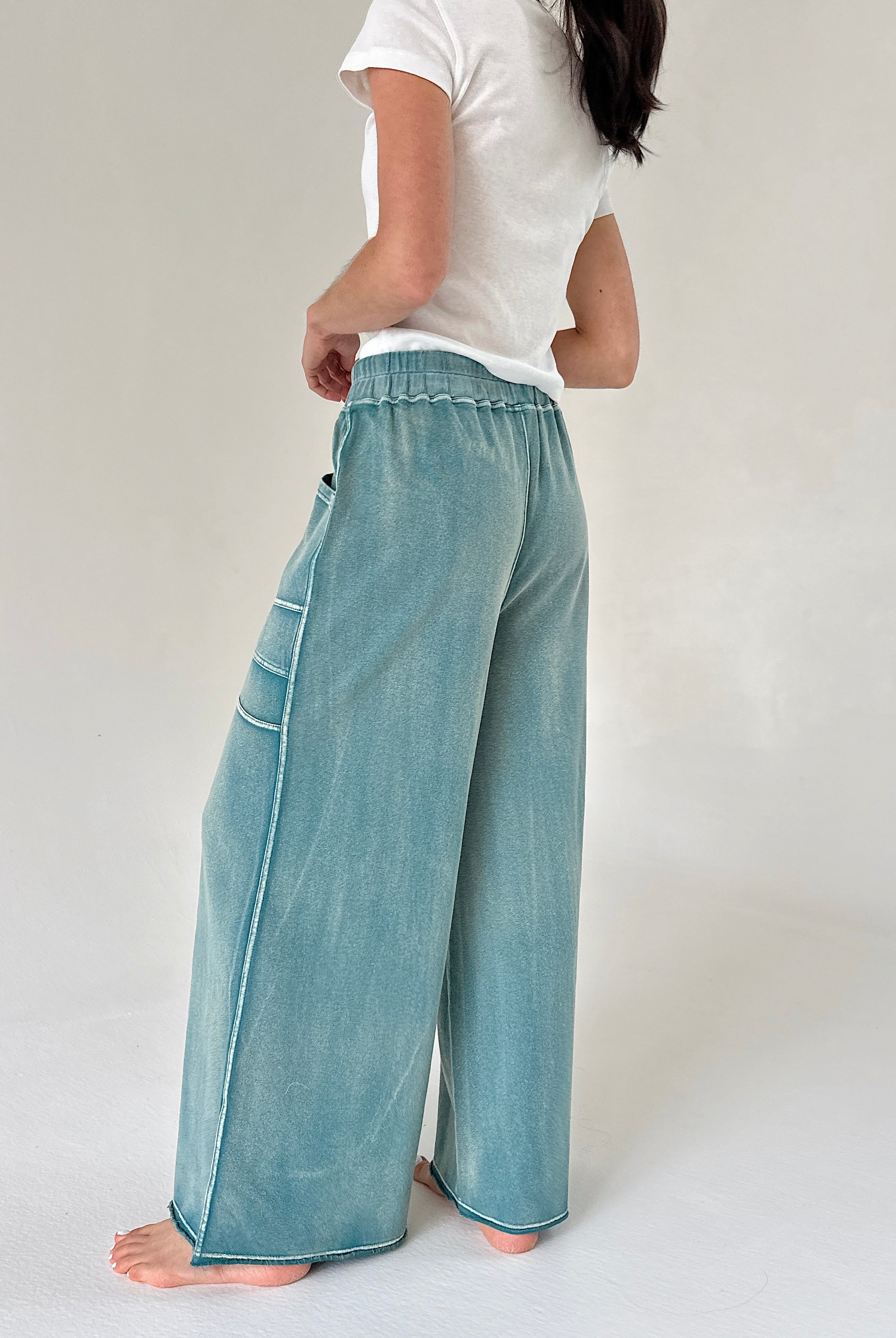 Person wearing teal wide-leg pants and a white shirt on a plain background