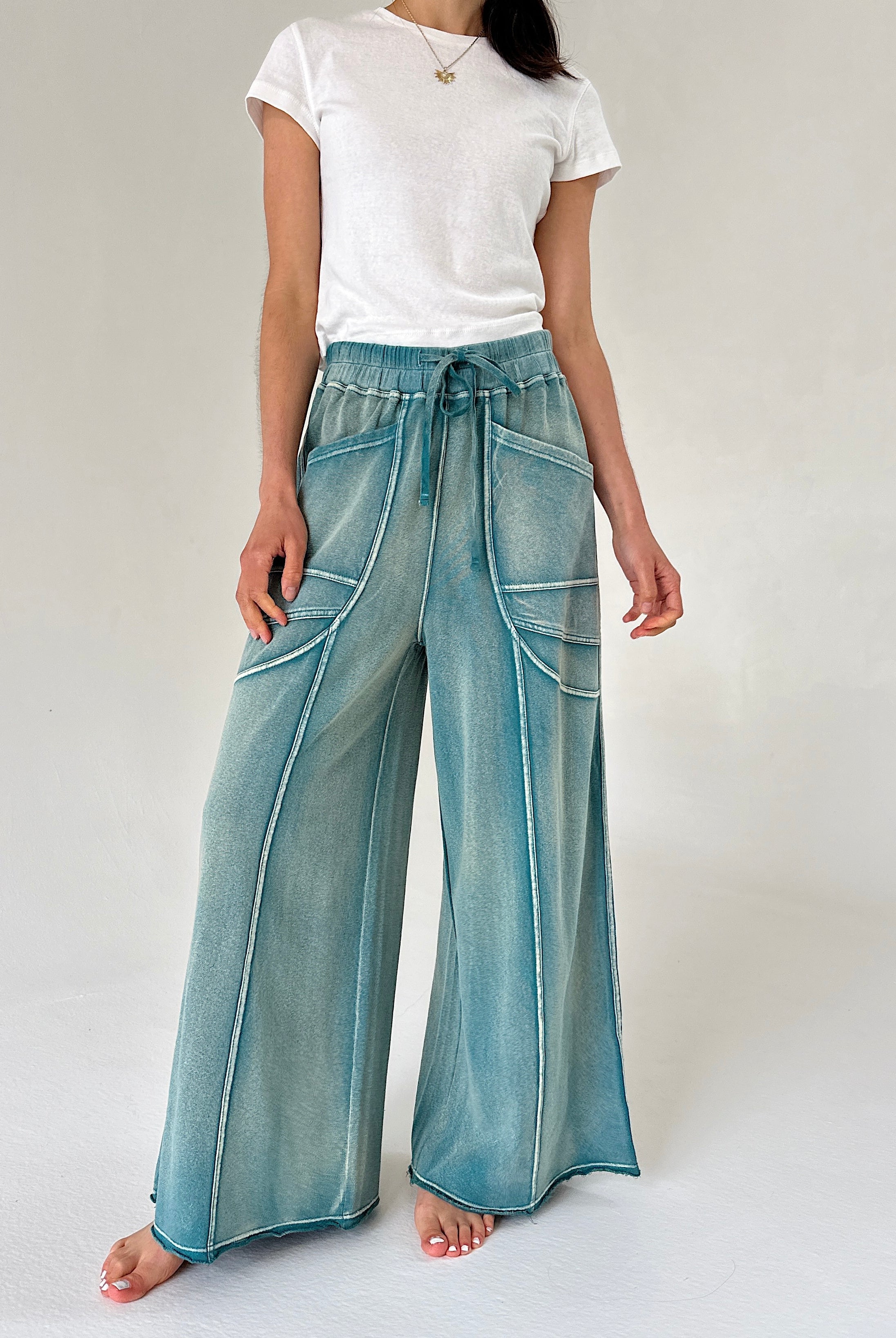 Person wearing teal wide-leg pants and a white t-shirt on a plain background