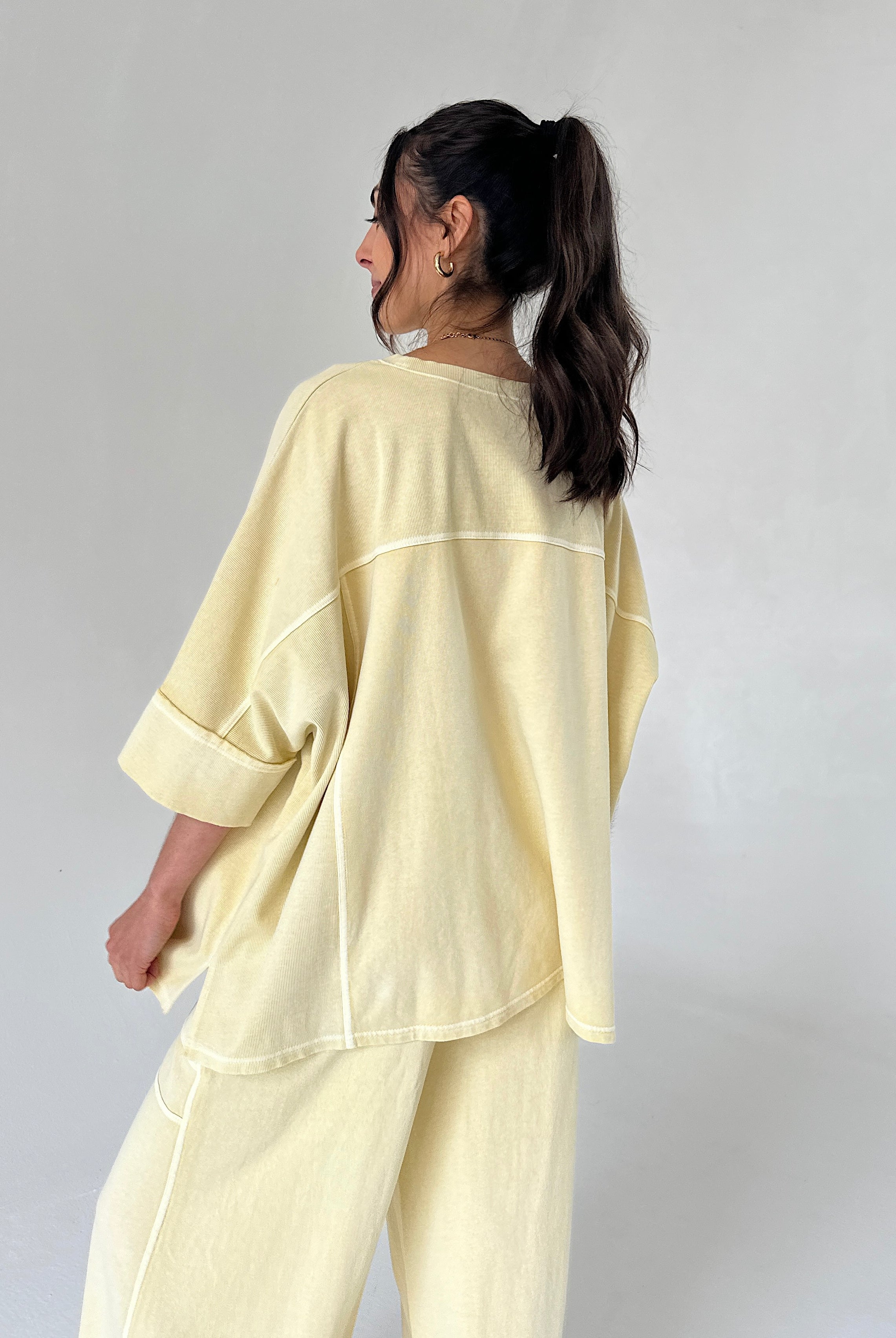 Woman wearing a light yellow outfit against a plain background from back