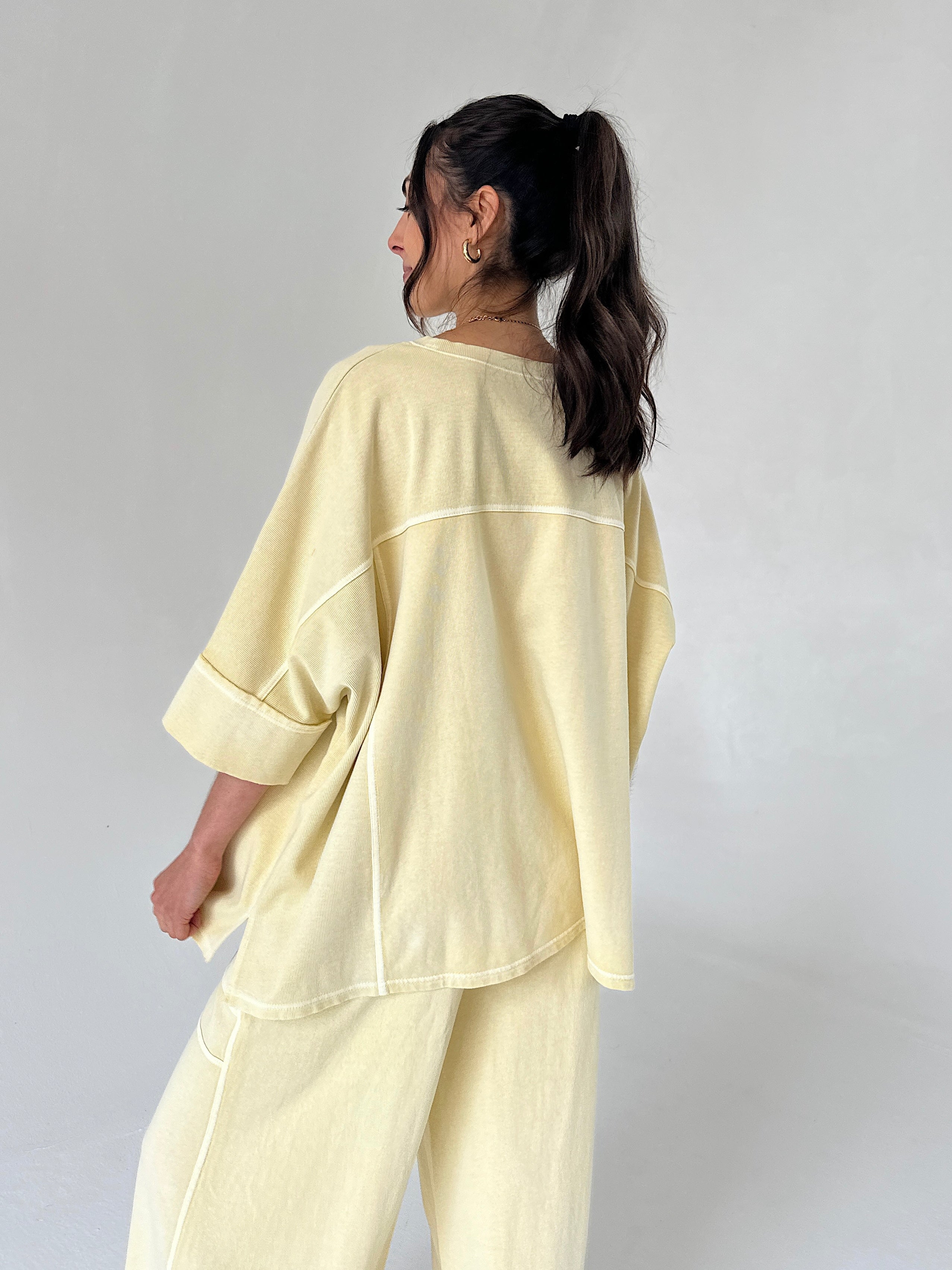 Woman wearing a light yellow outfit against a plain background from back