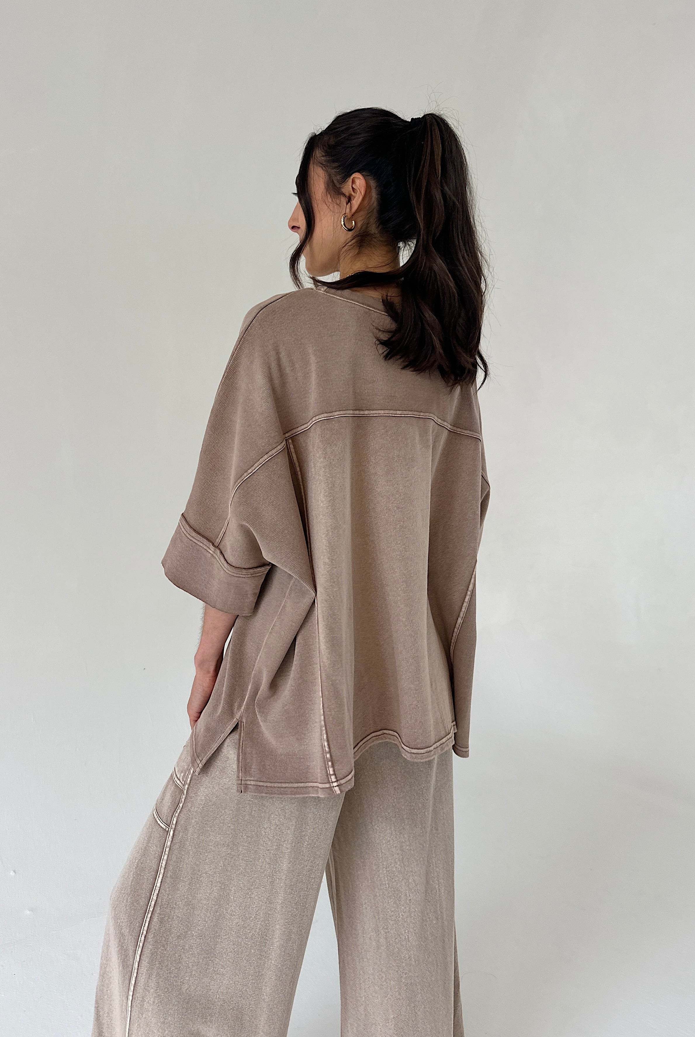Person wearing a brown top and matching pants against a plain background from back