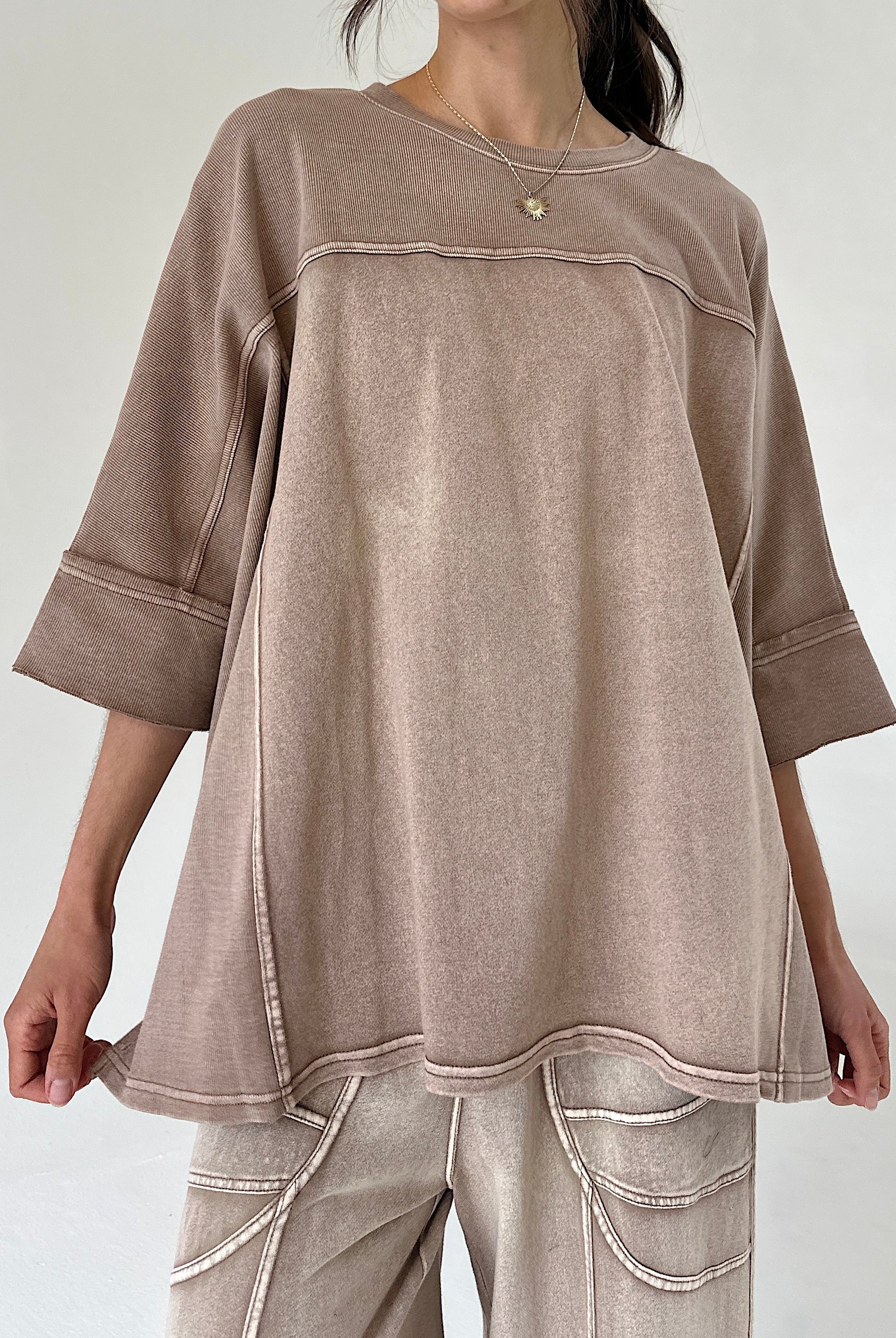 Person wearing a brown oversized top with a plain background