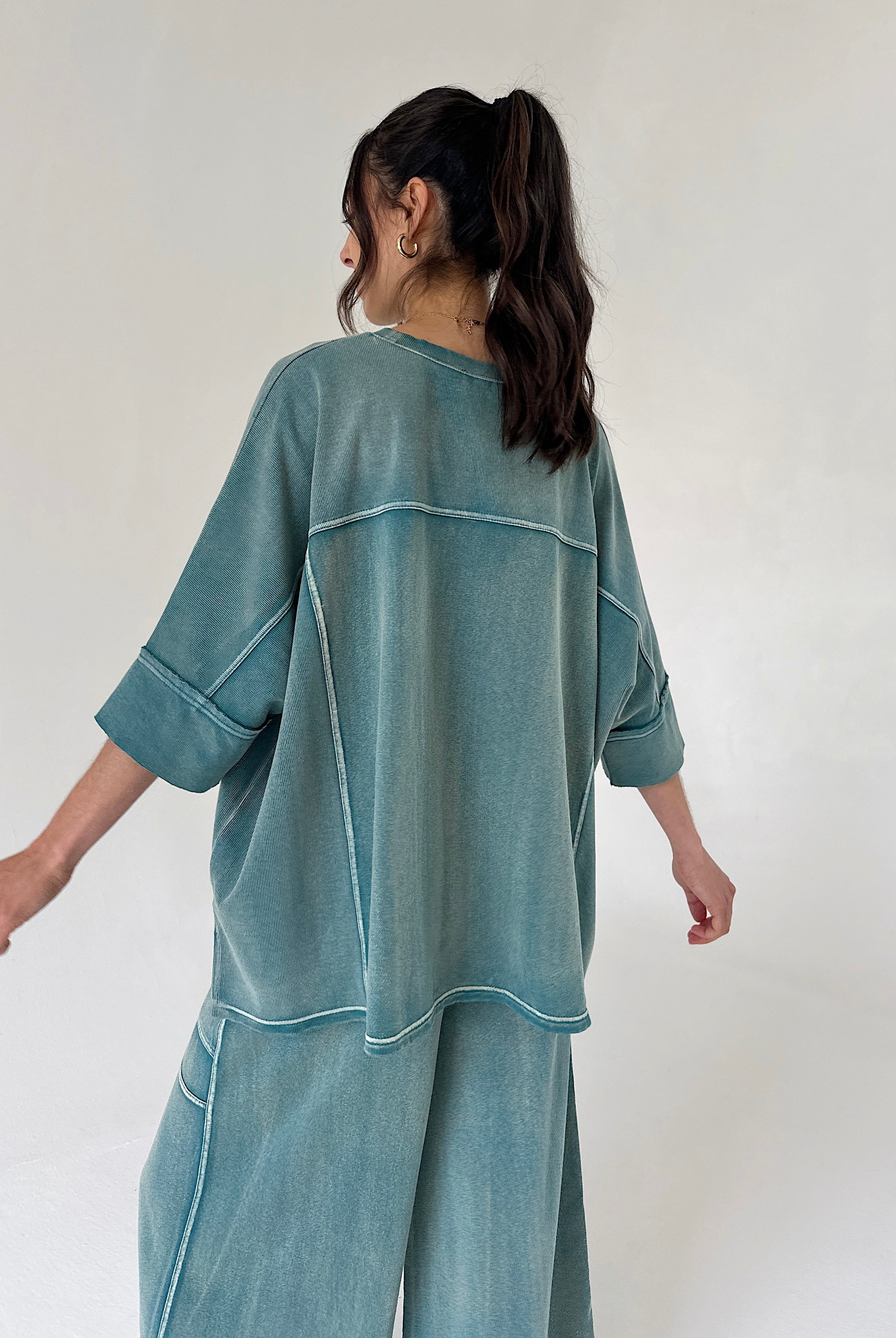 Person wearing a teal oversized shirt and pants set against a white background