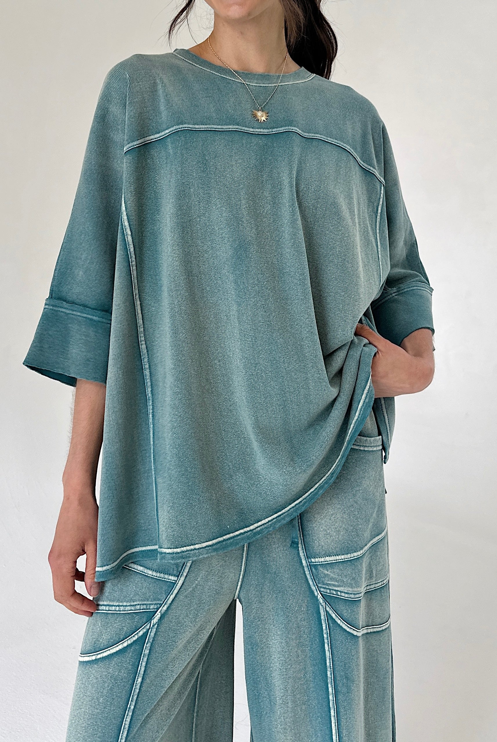Person wearing a teal oversized top and pants set on a plain background