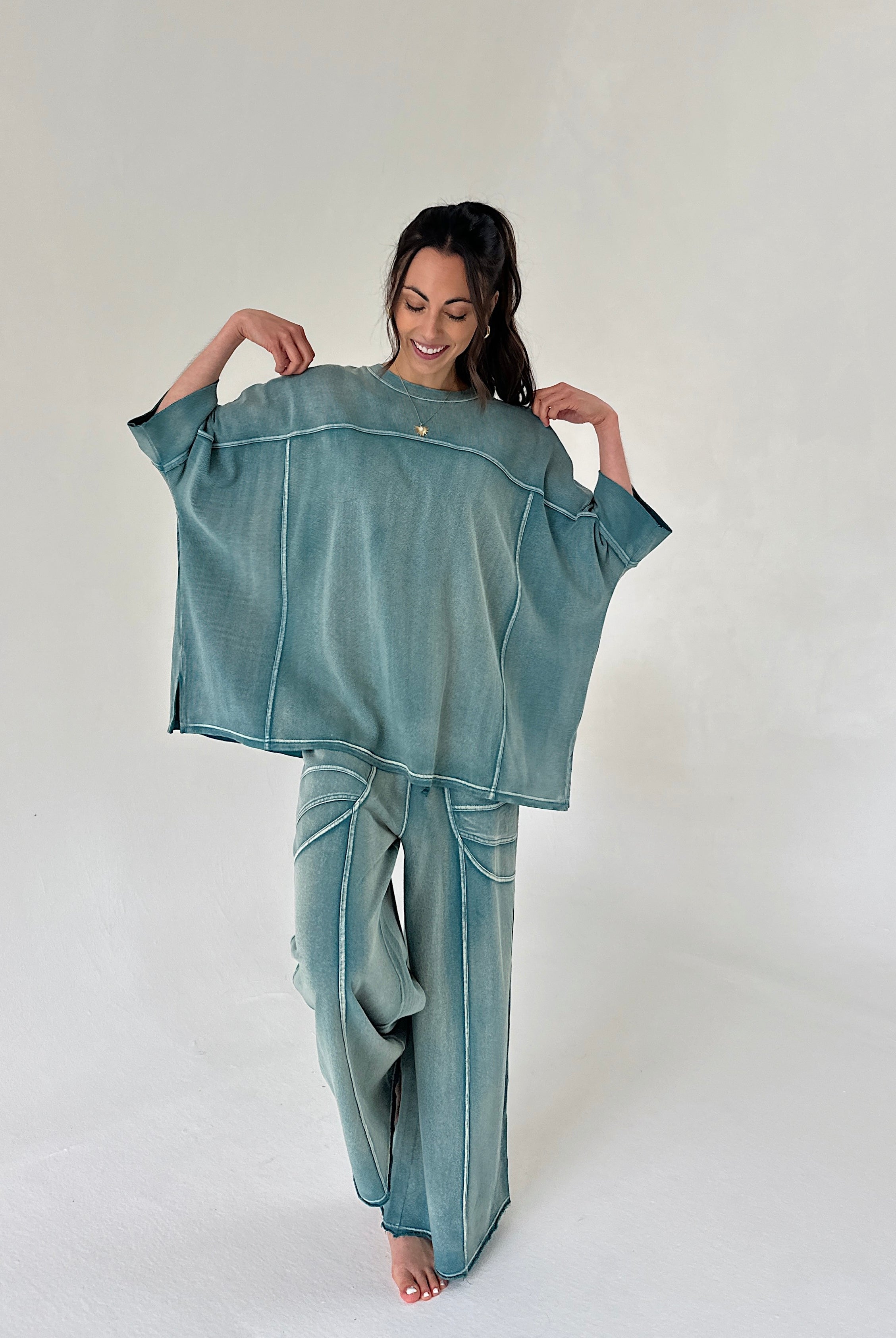 Woman wearing a teal oversized shirt and pants set on a plain background