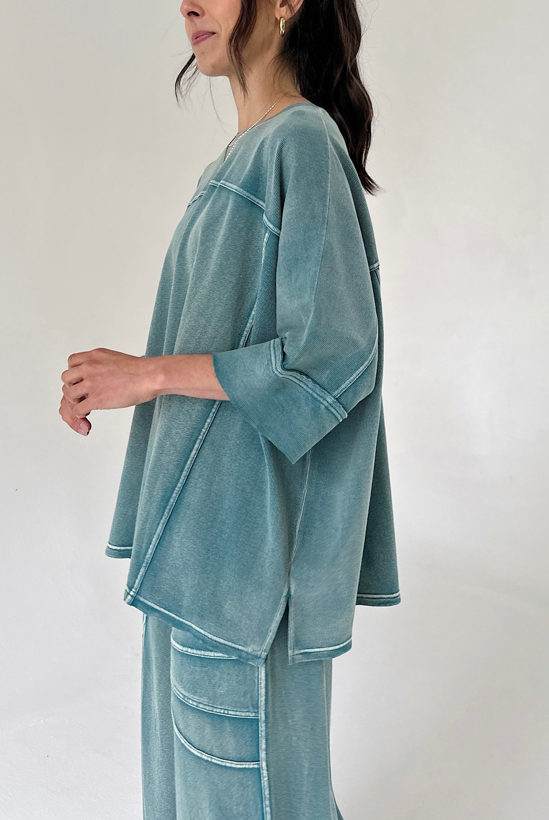 Woman wearing a teal outfit against a white background from side
