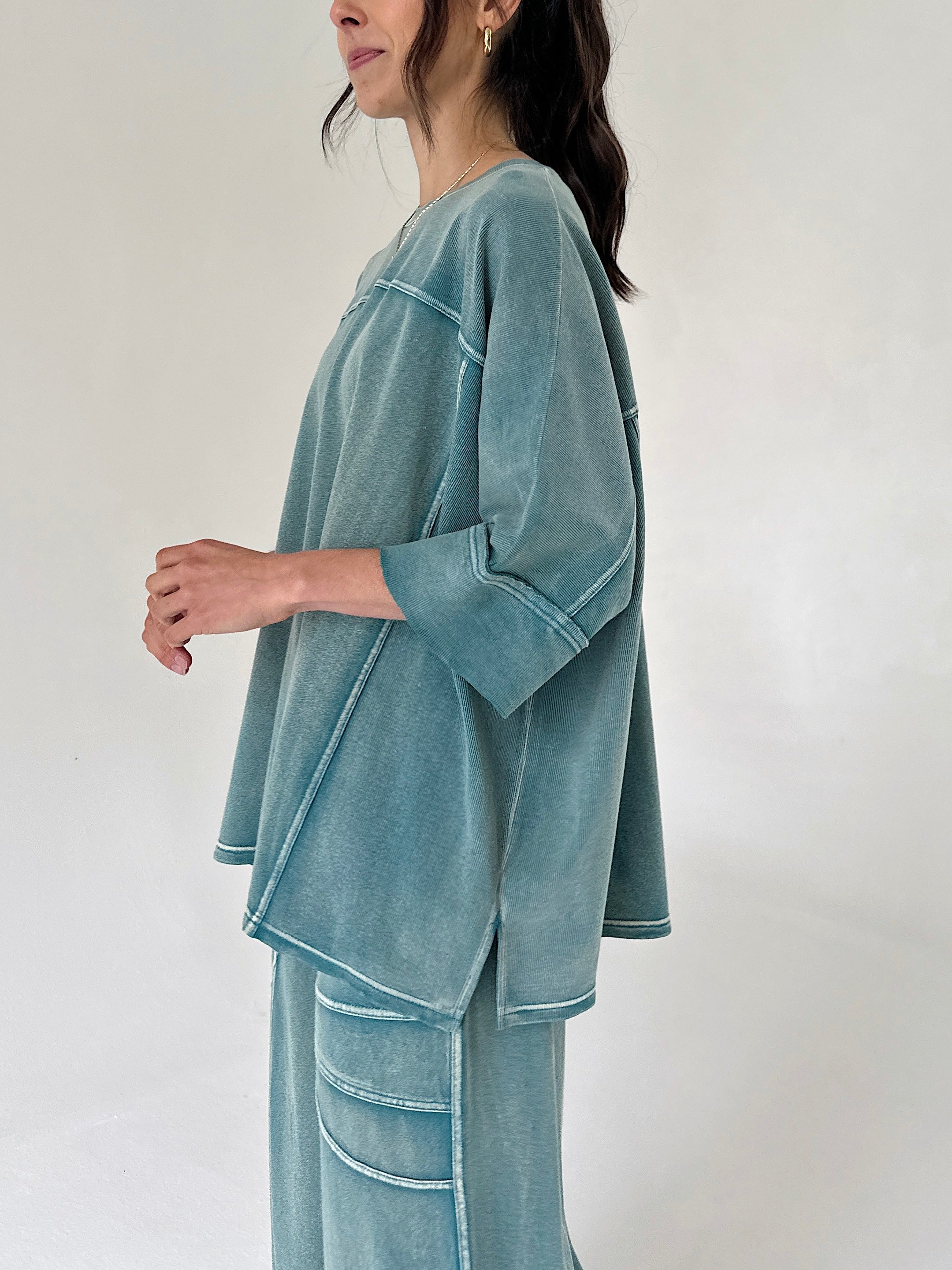 Woman wearing a teal outfit against a white background from side