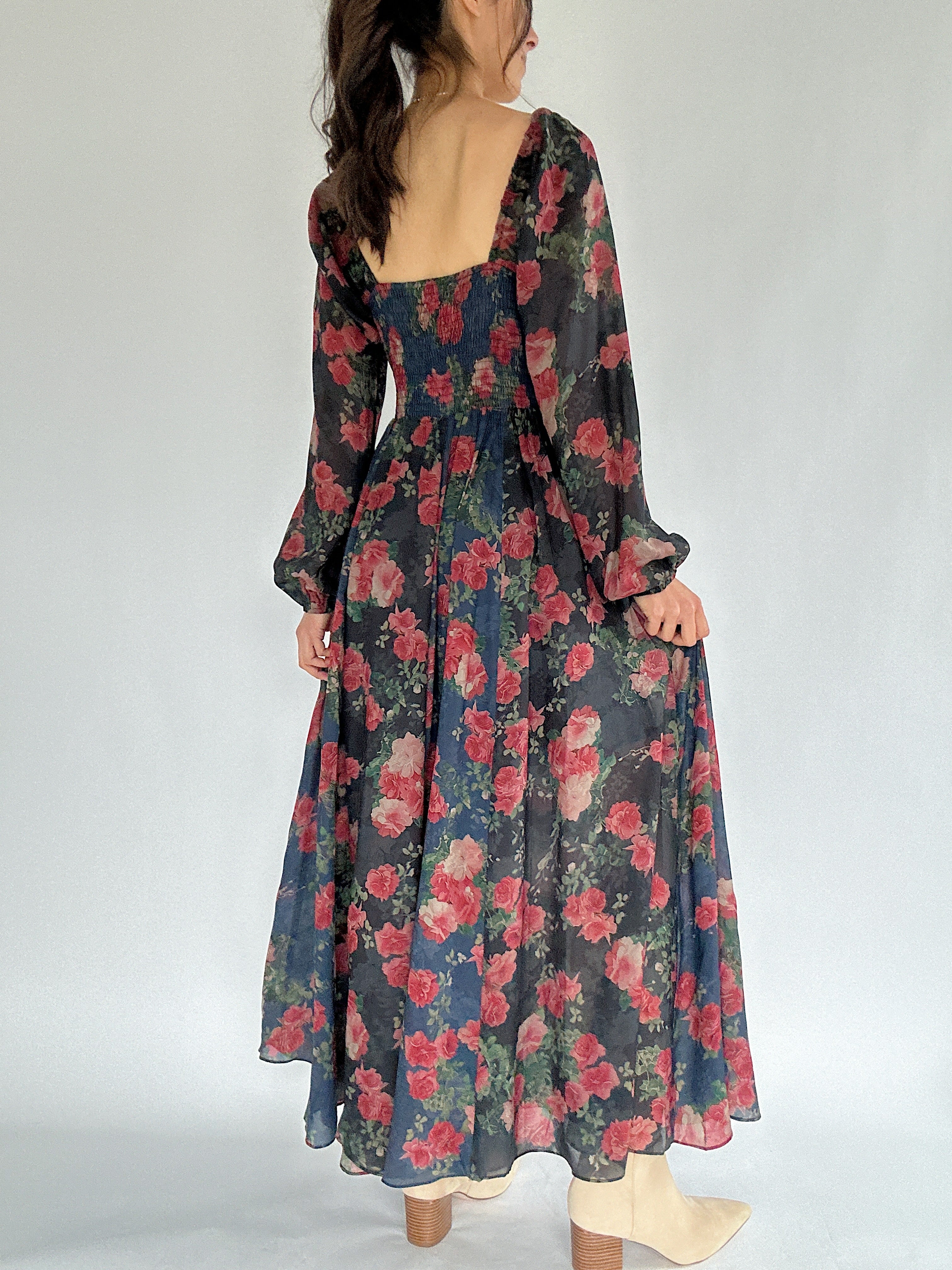 Woman wearing a floral dress with a plain background showing back view