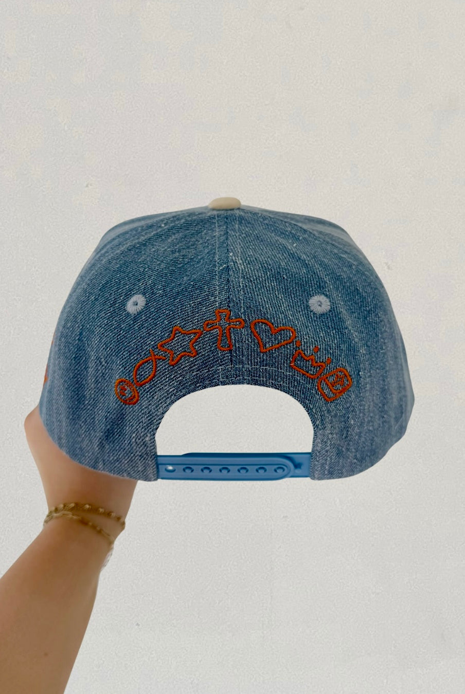 Denim cap with embroidered design held by a hand against a plain background