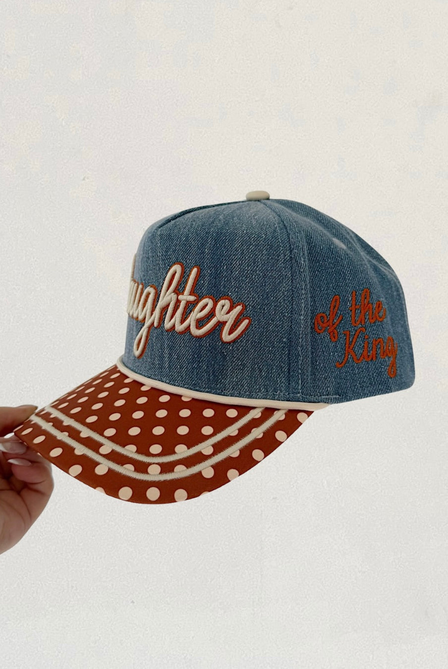 Denim cap with polka dot brim and embroidered text on a white background