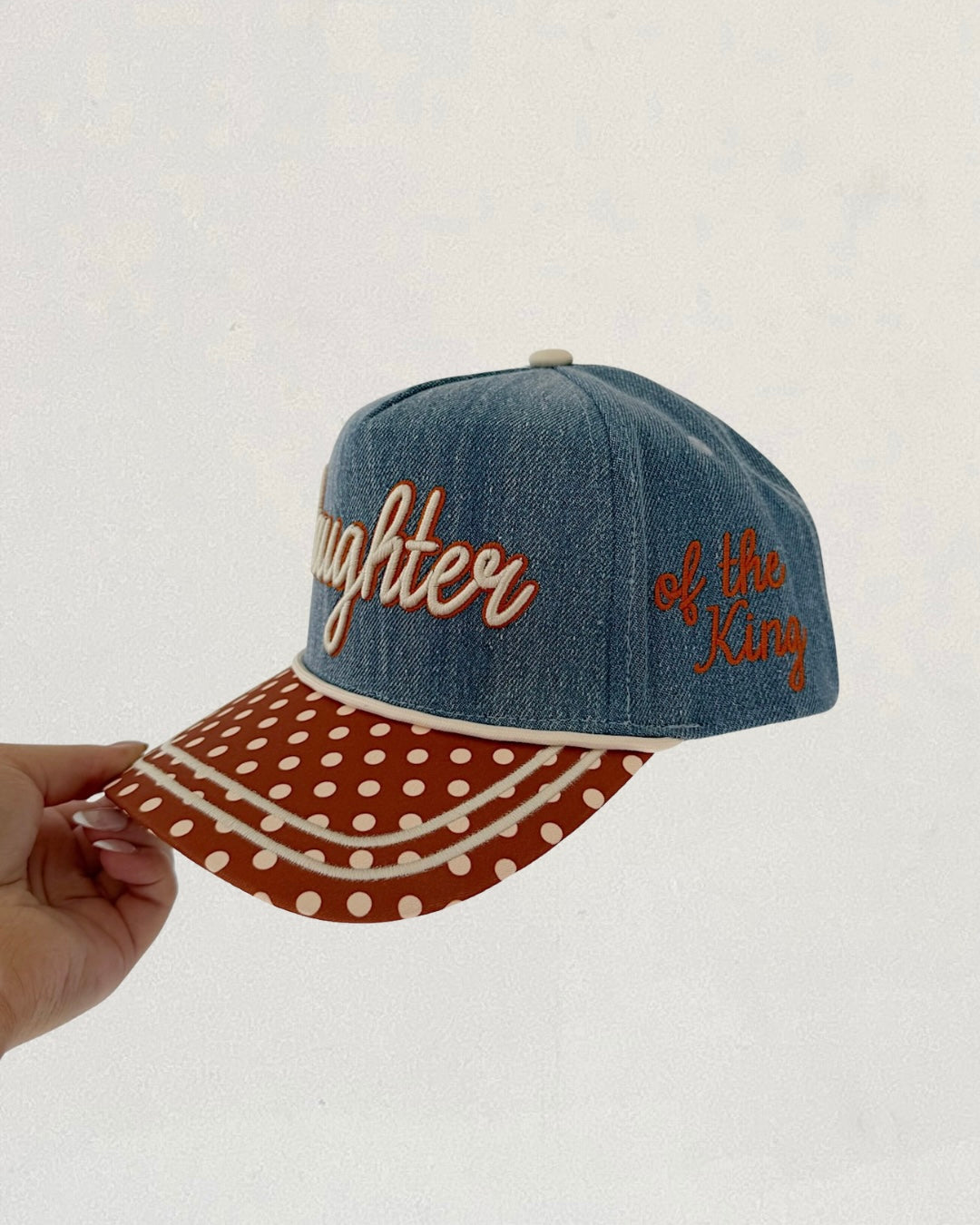 Denim cap with polka dot brim and embroidered text on a white background