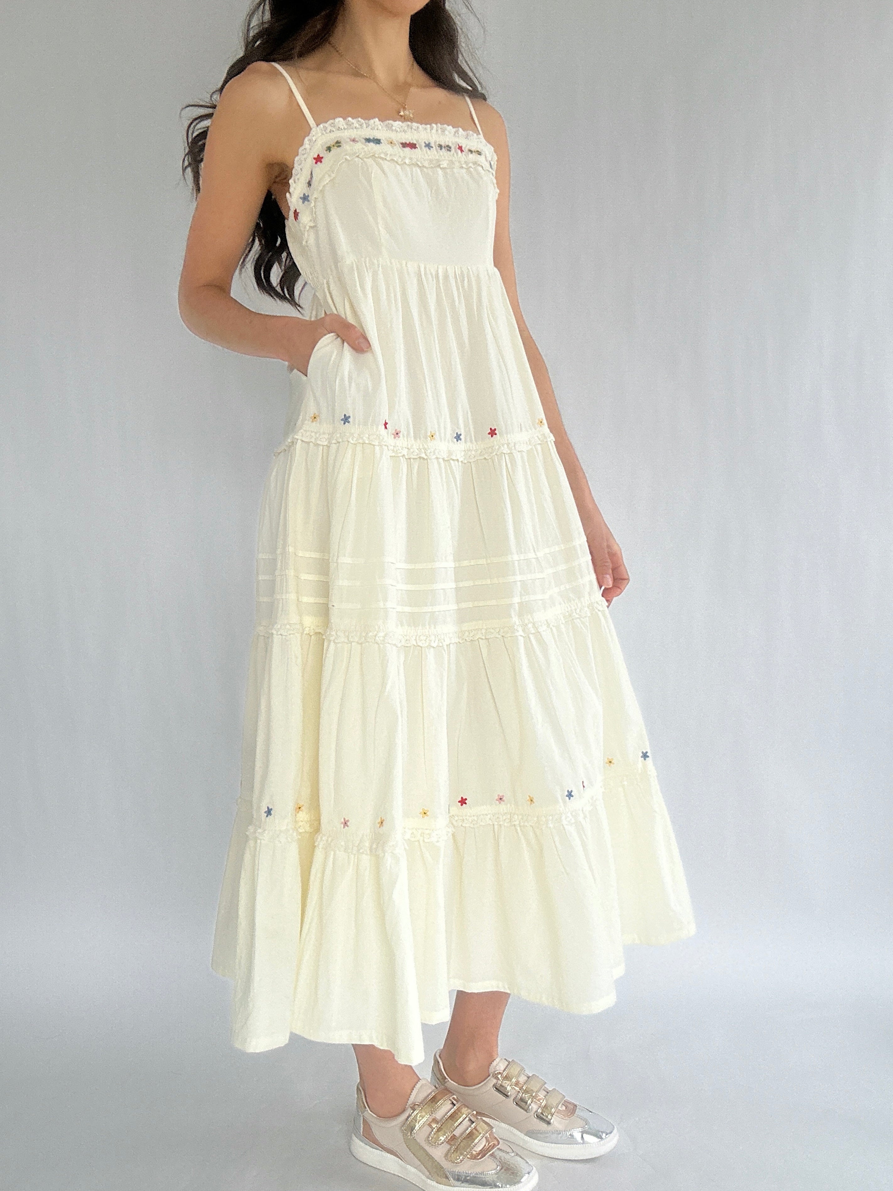 Woman wearing a white dress with floral embellishments on a plain background showing the side pockets