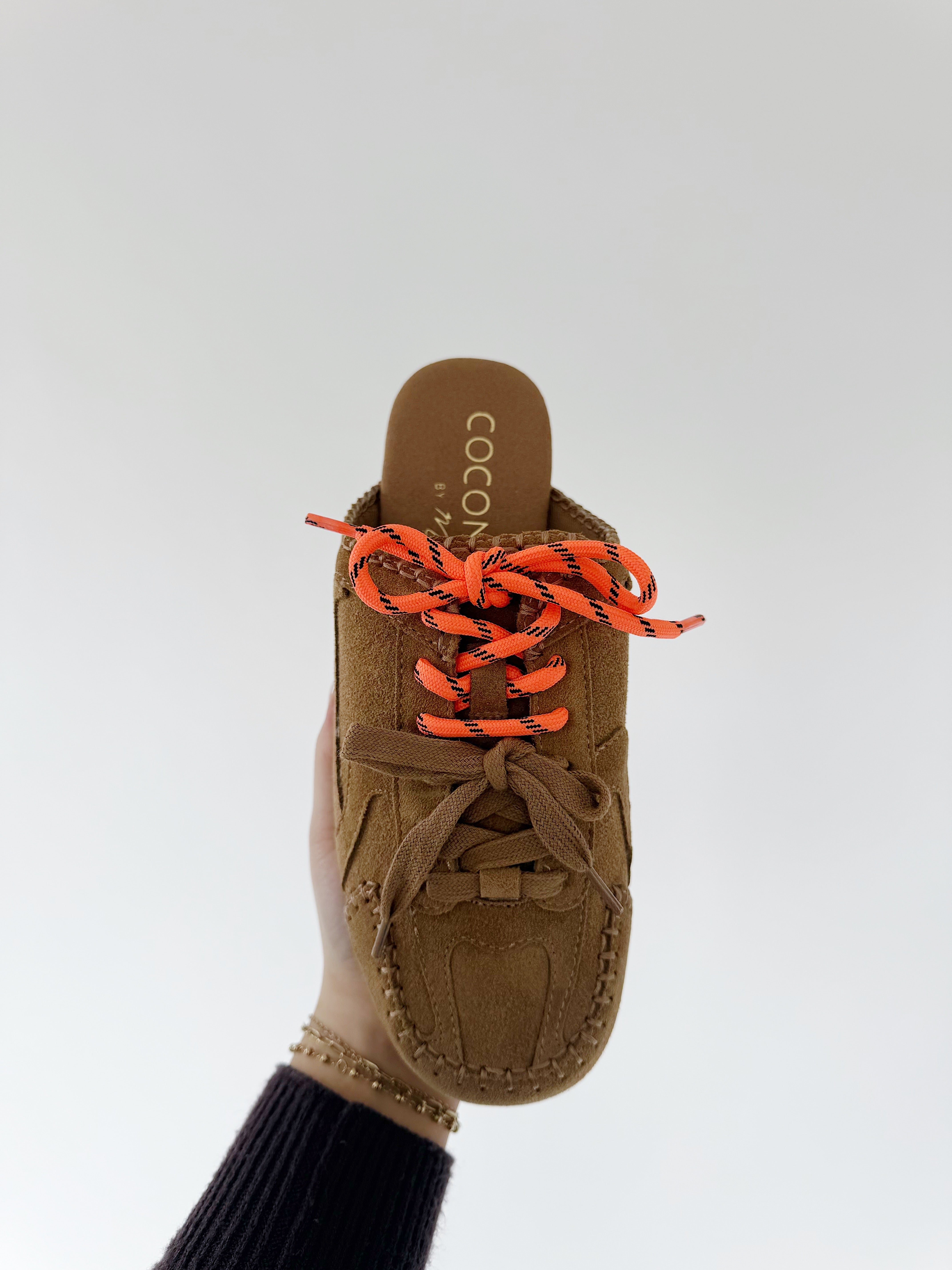 Brown moccasin slide shoe with orange laces on a white background