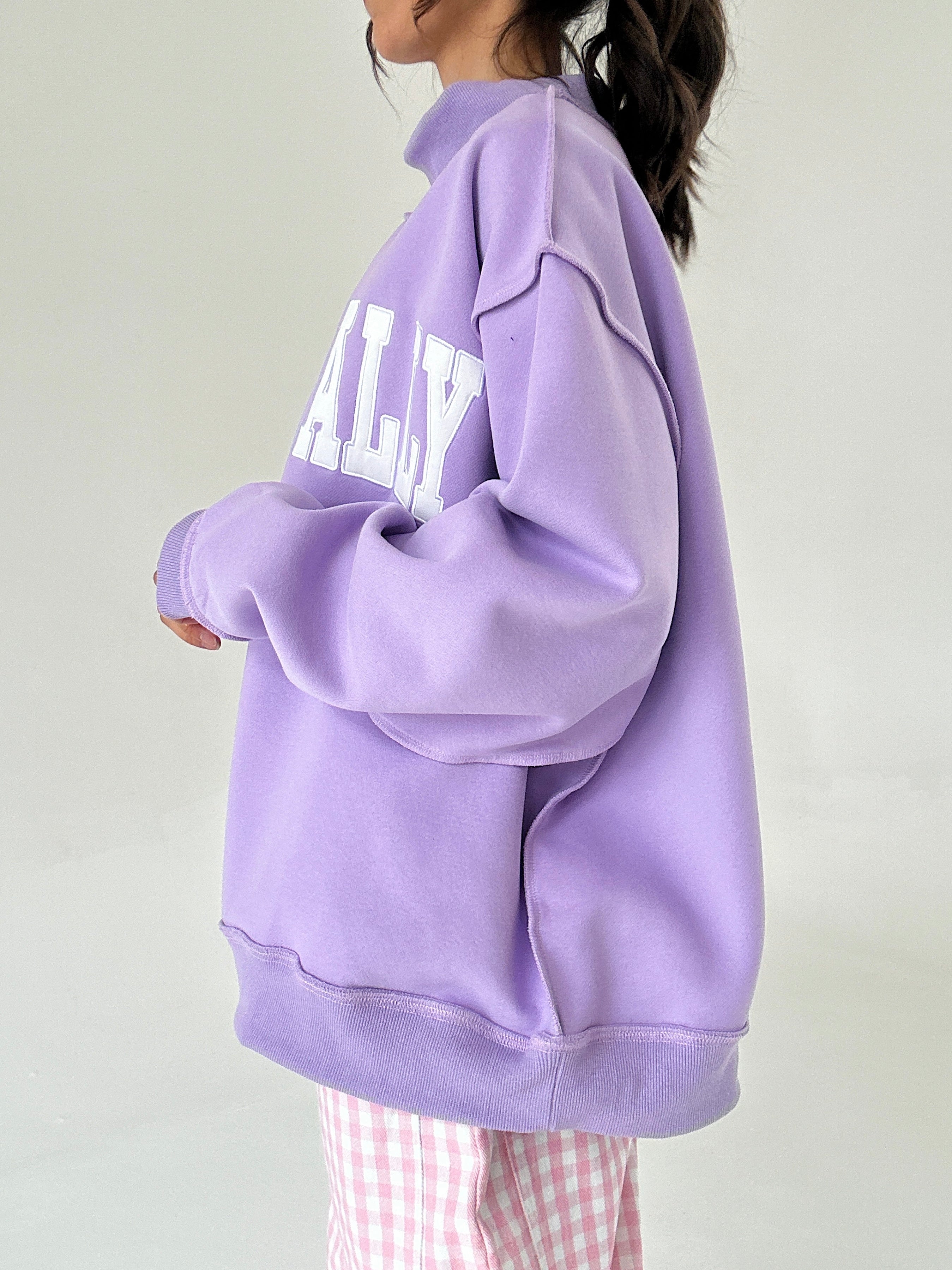 Person wearing a purple oversized mockneck with text on a plain background