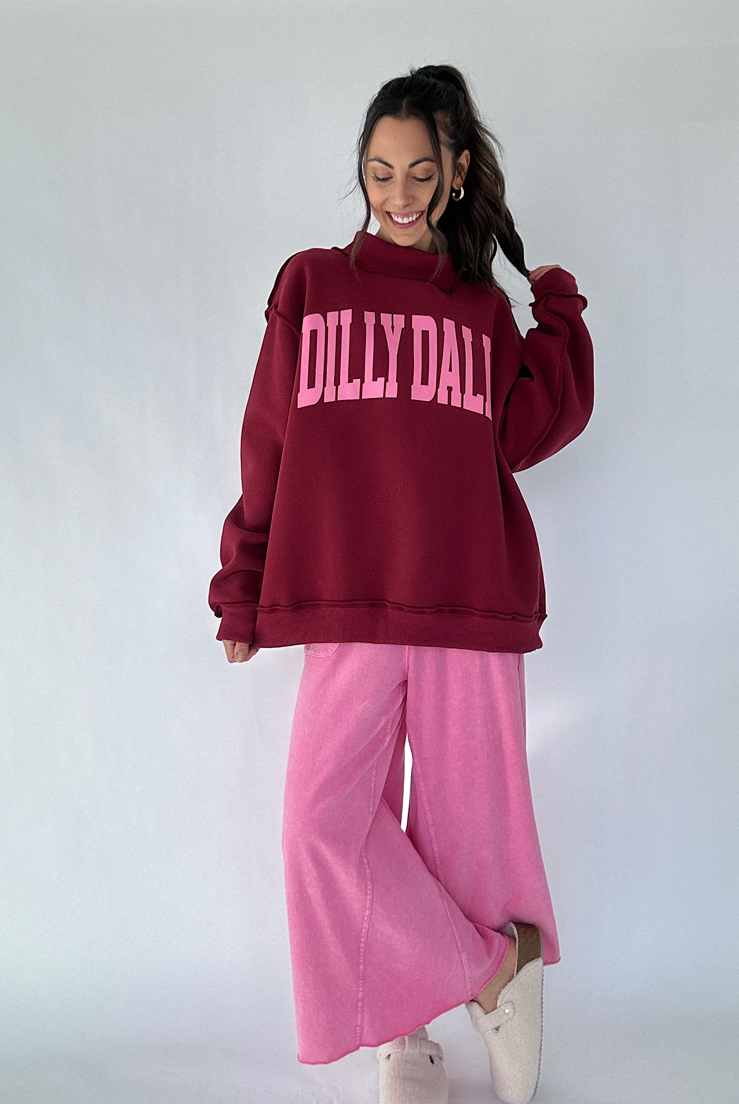 Person wearing a maroon 'Dilly Dally' mock neck pullover and pink pants on a white background