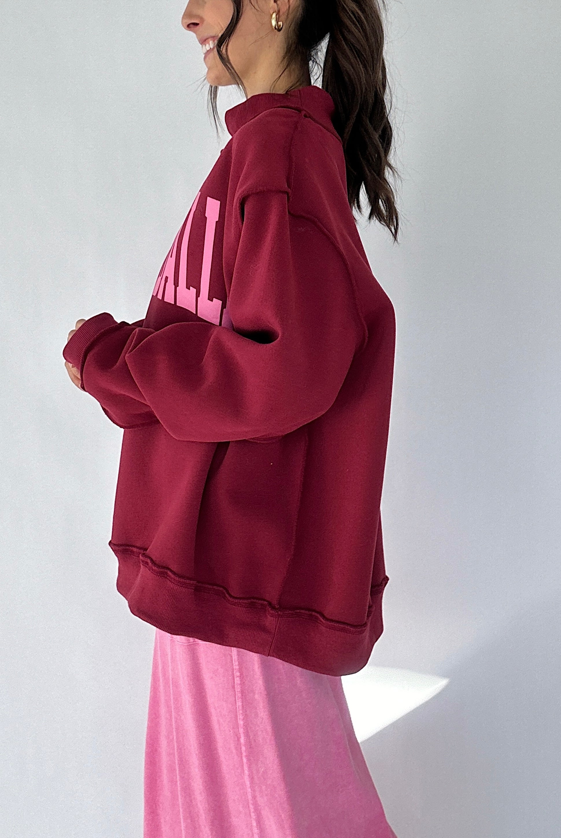 Person wearing a maroon mock neck with pink text on a white background from side
