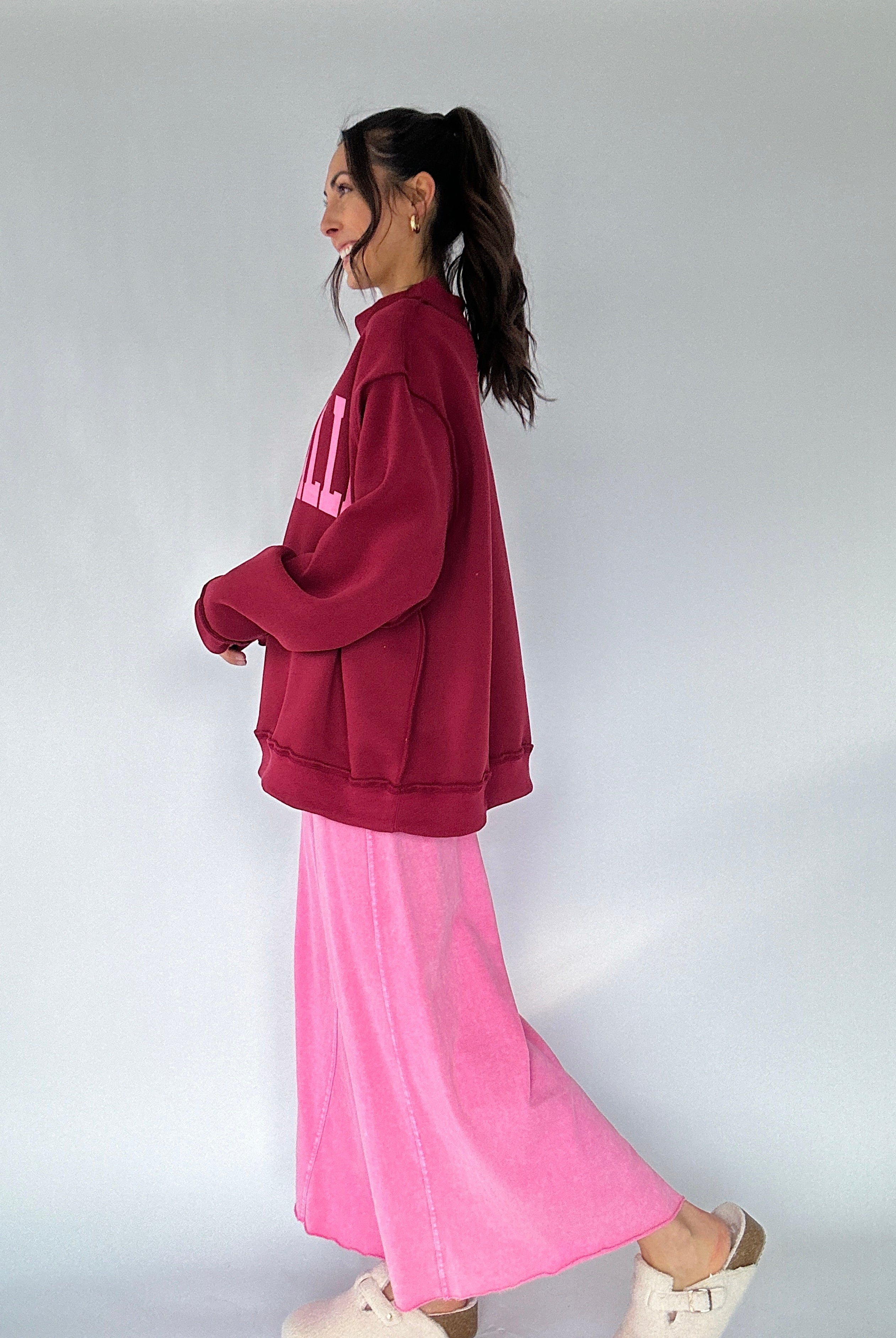 Person wearing a maroon mock neck and pink pants on a plain background from side