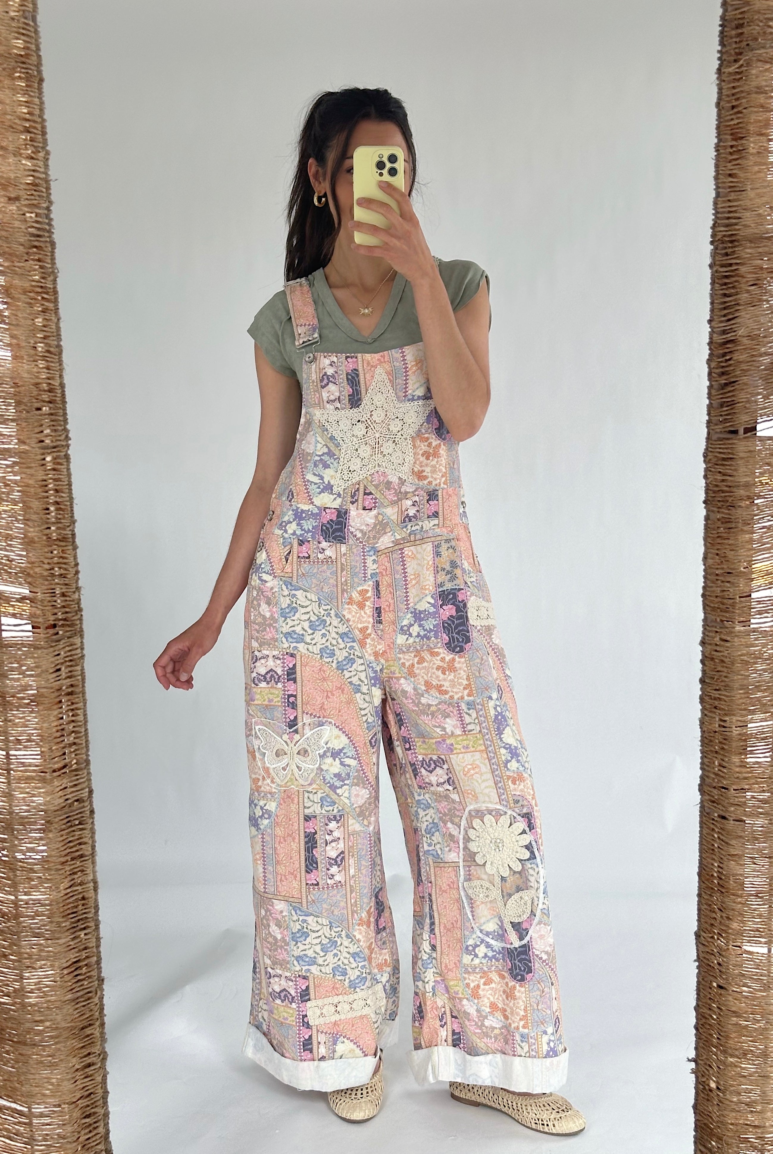 Person wearing a floral patchwork overalls over a green t-shirt taking a selfie in the mirror