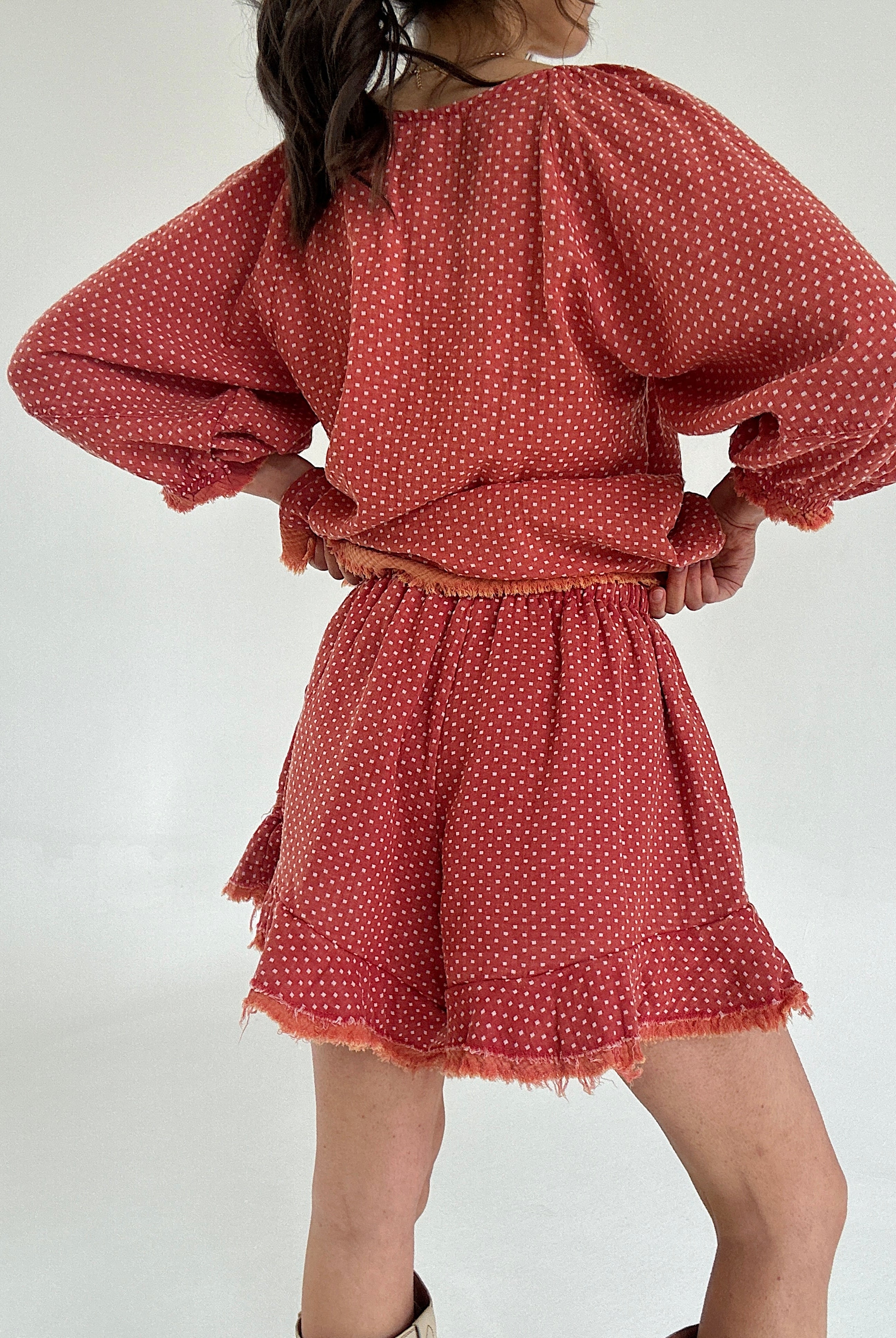 Person wearing a red polka dot set with ruffle shorts from back on a white background