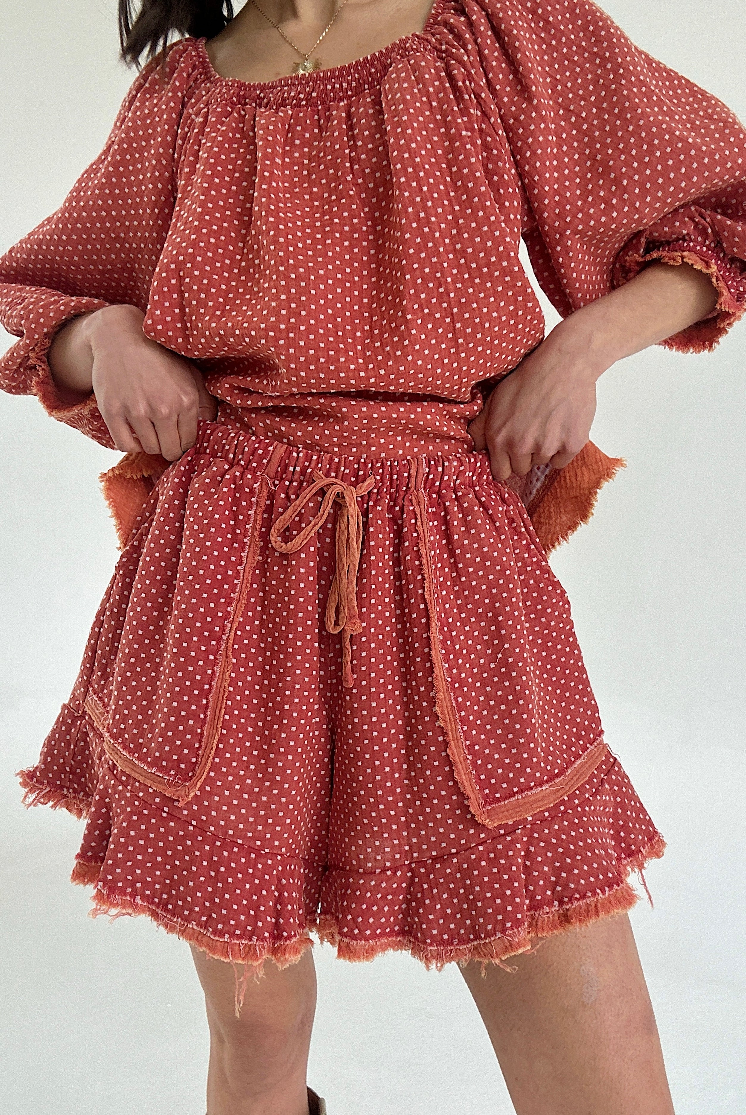 Person wearing a rust-colored polka dot set with ruffle shorts on a white background