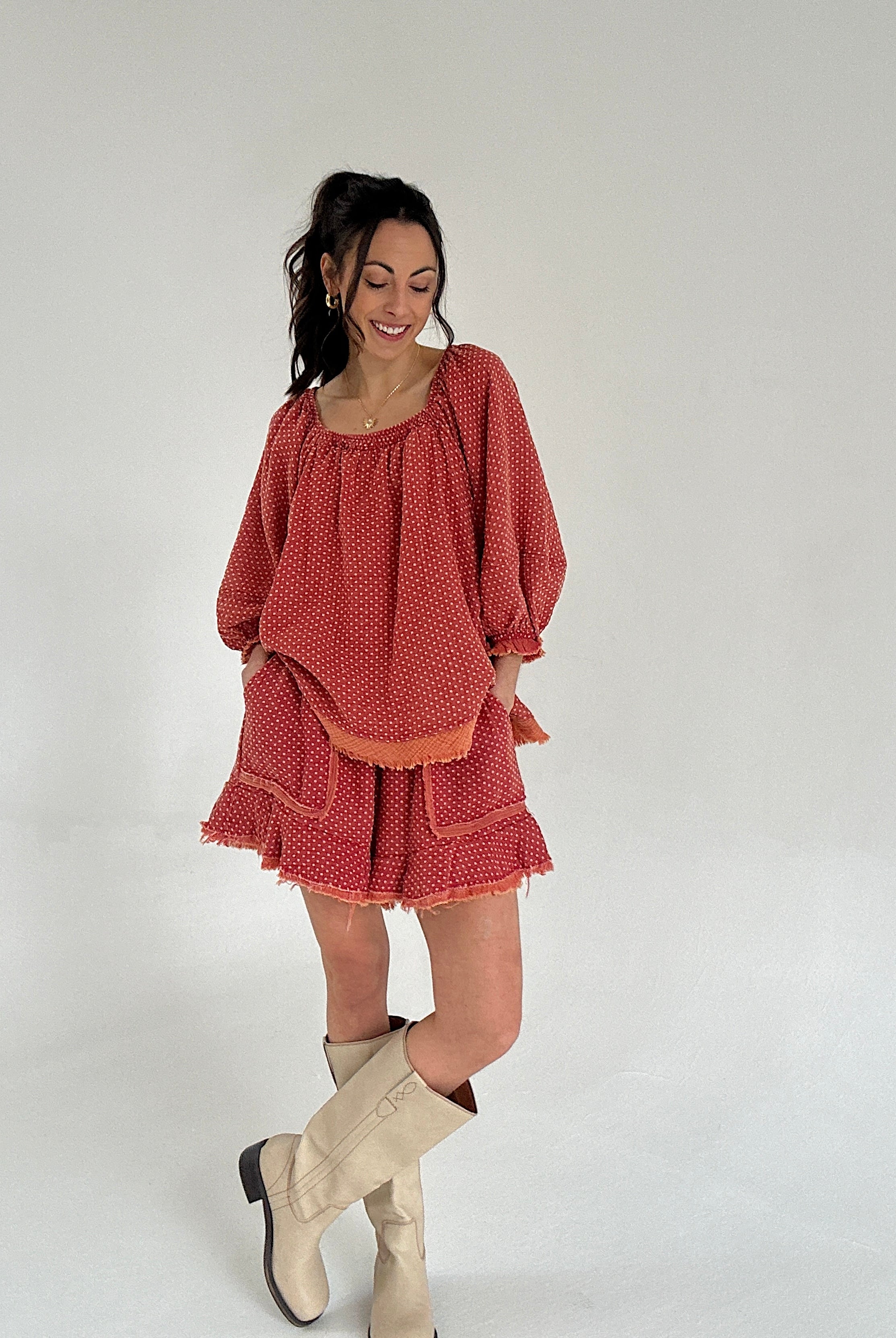 Woman wearing a red polka dot set and beige boots on a white background