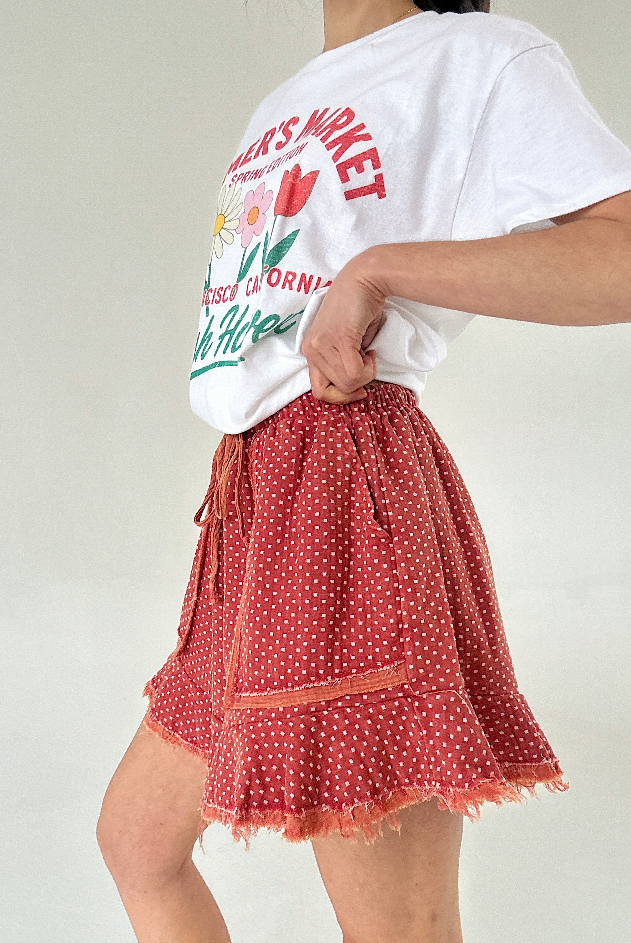 Person wearing a white t-shirt with graphics and a red polka dot short on a plain background