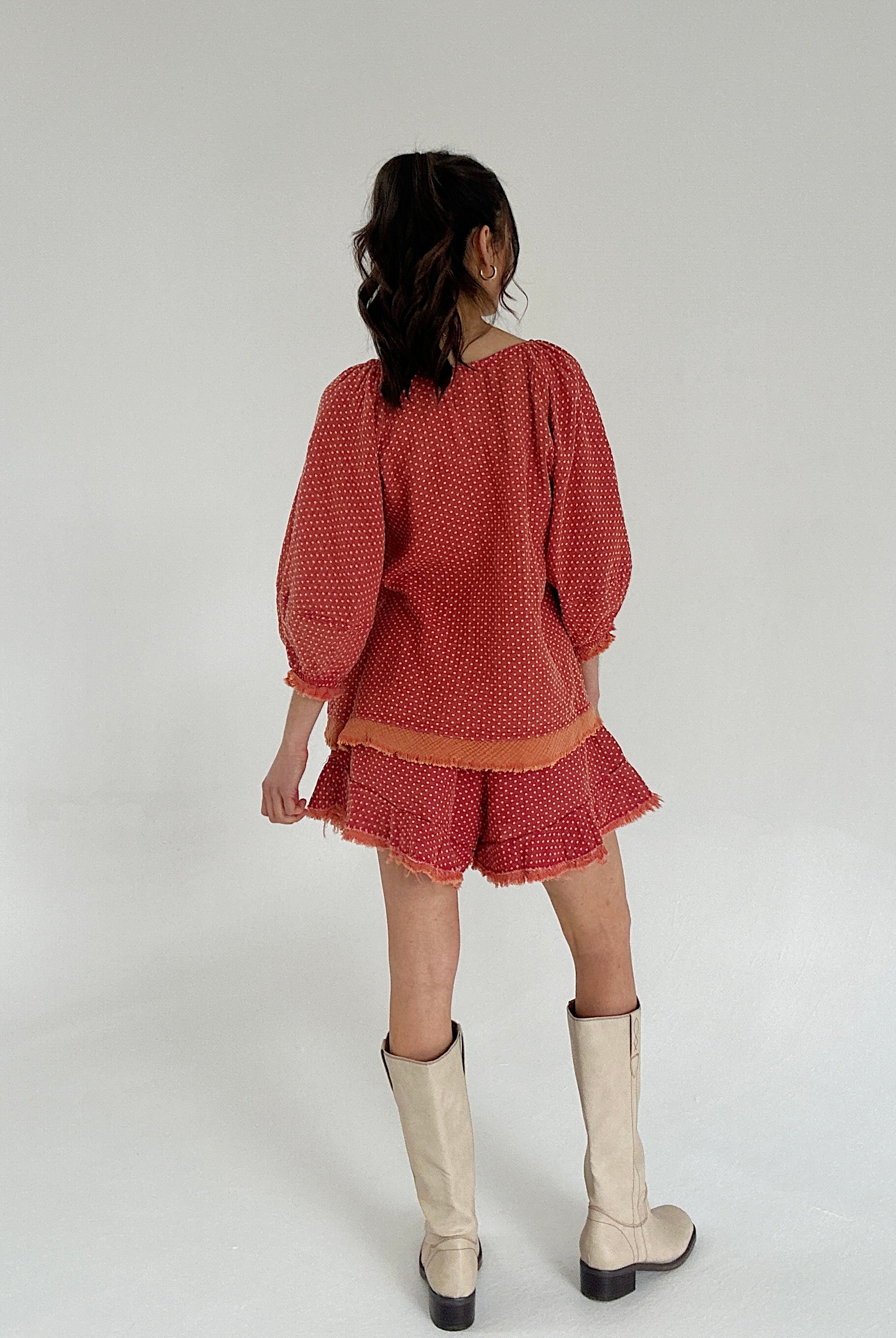 Person wearing a red dotted set with white boots on a plain background showing back