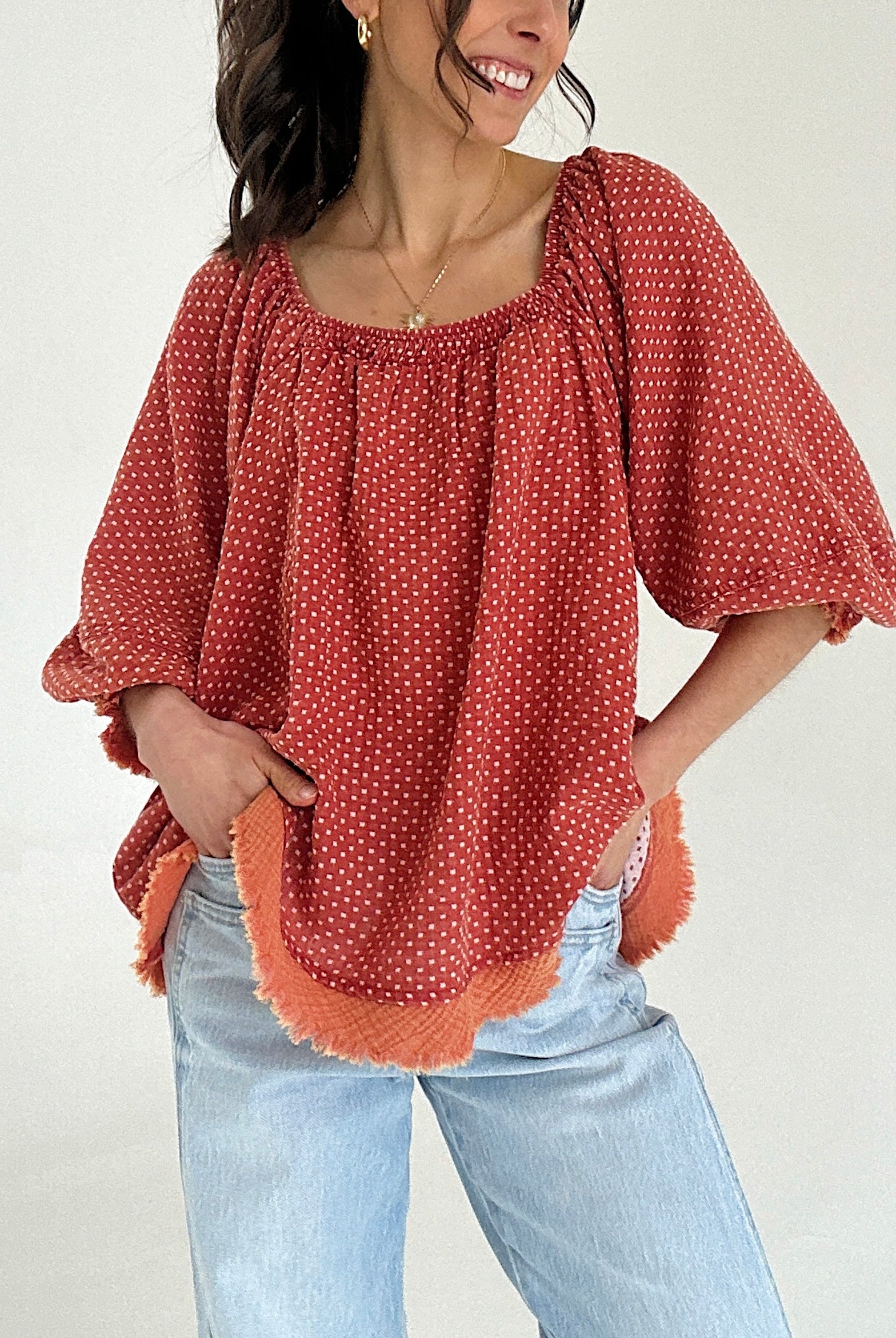 Woman wearing a rust-colored blouse with white polka dots and light blue jeans against a plain background