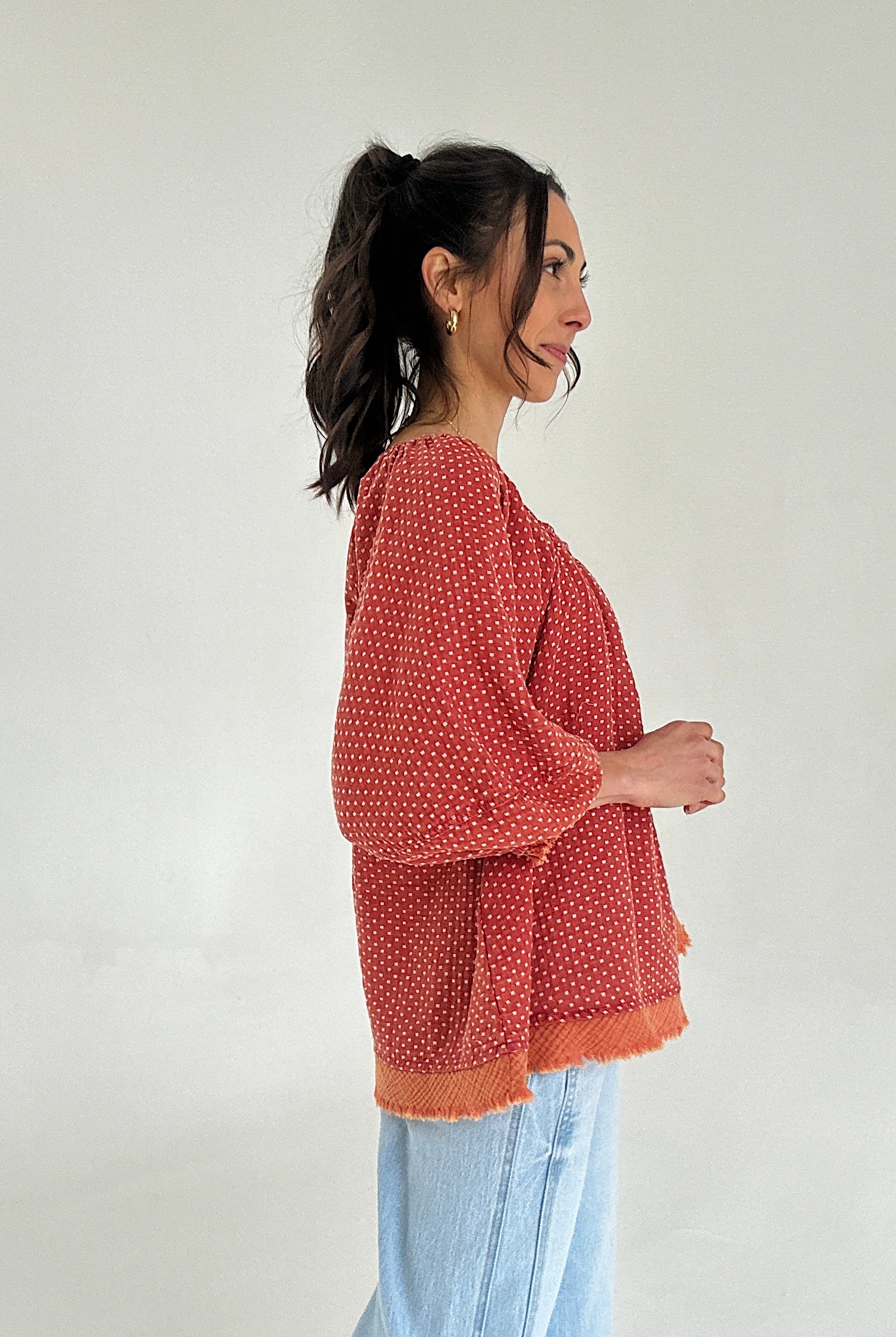 Woman wearing a red patterned top against a white background from side