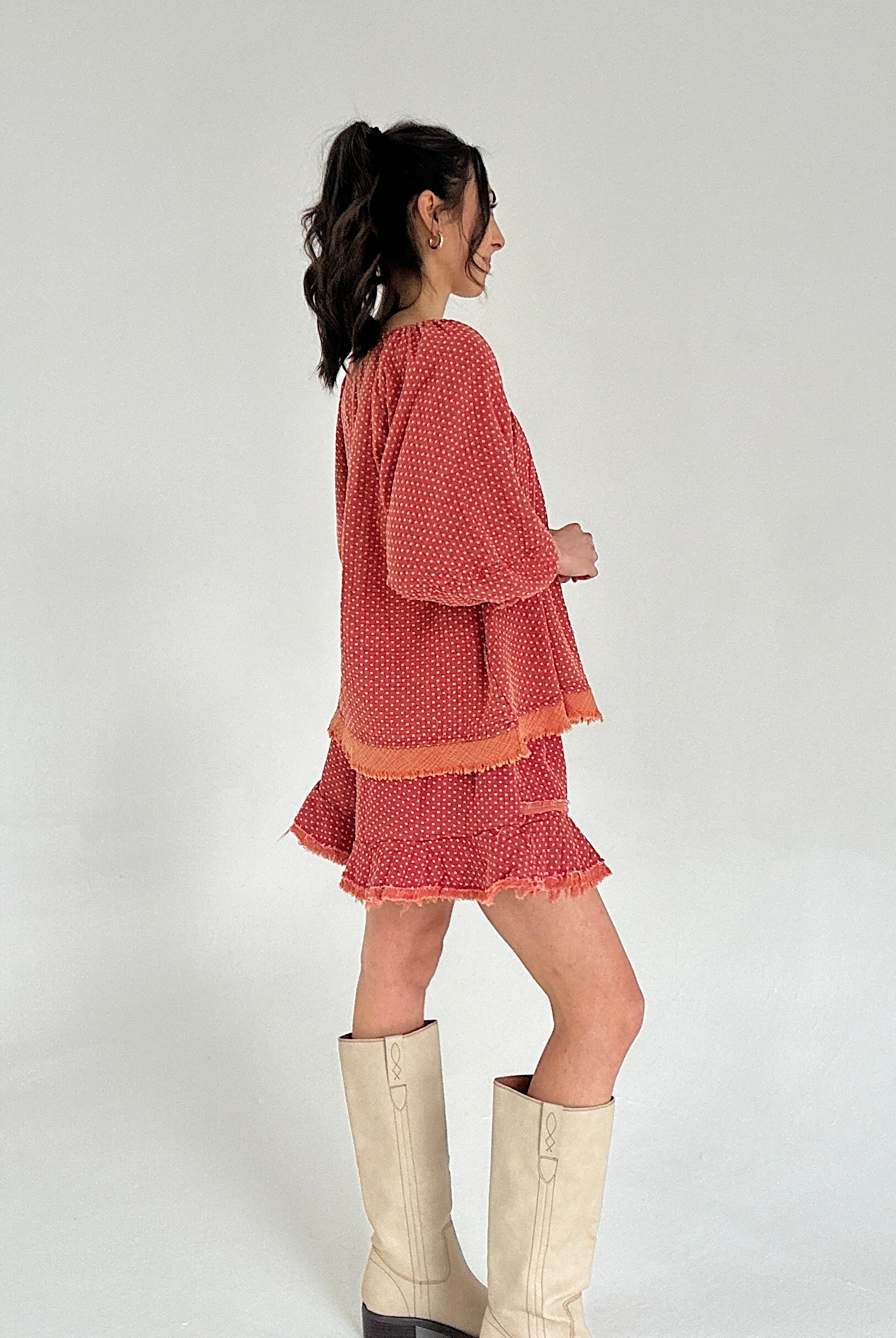 Woman wearing a red set with ruffled layers and white boots on a plain background