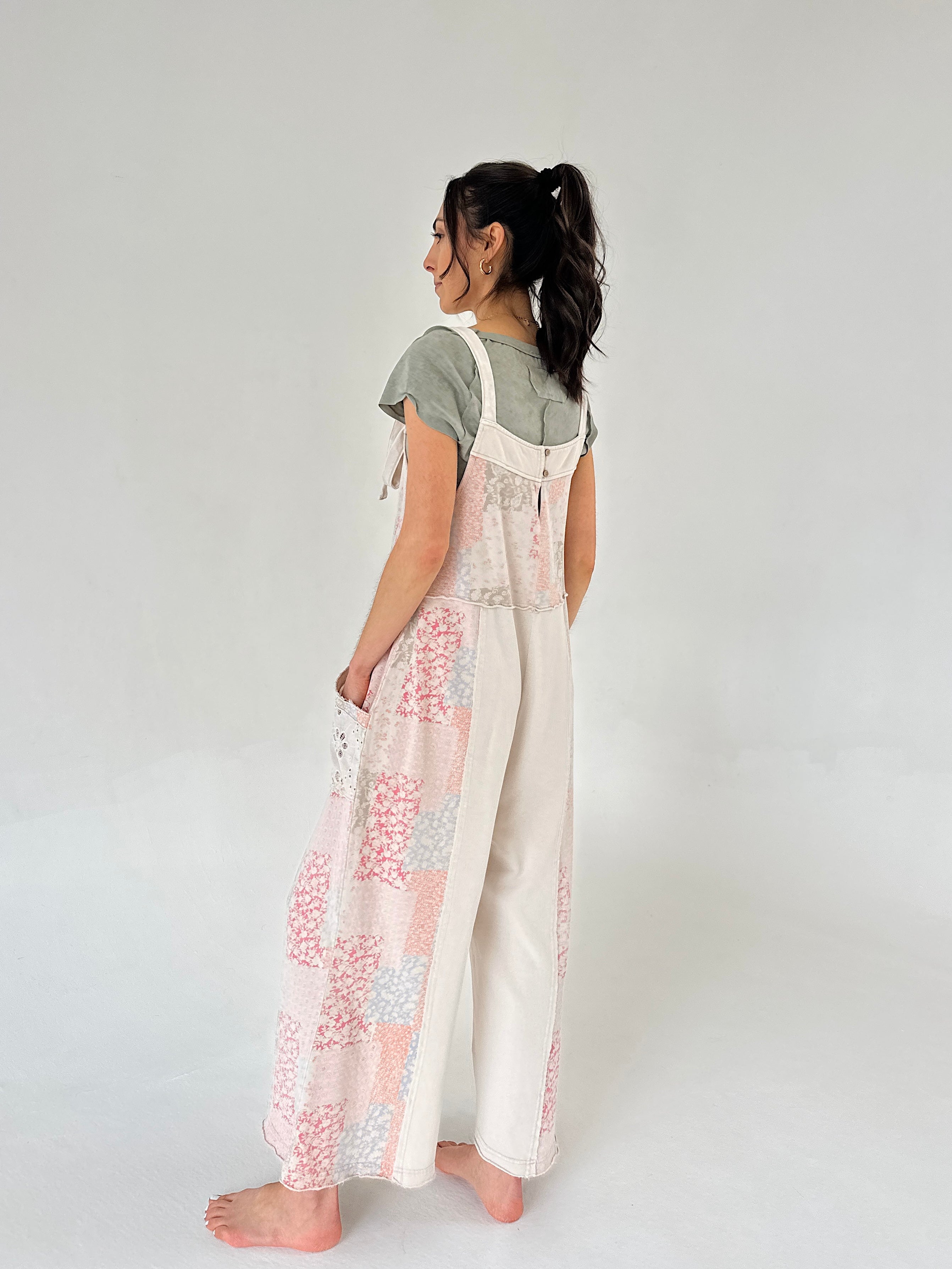 Woman wearing a floral overalls and green top on a plain background from back