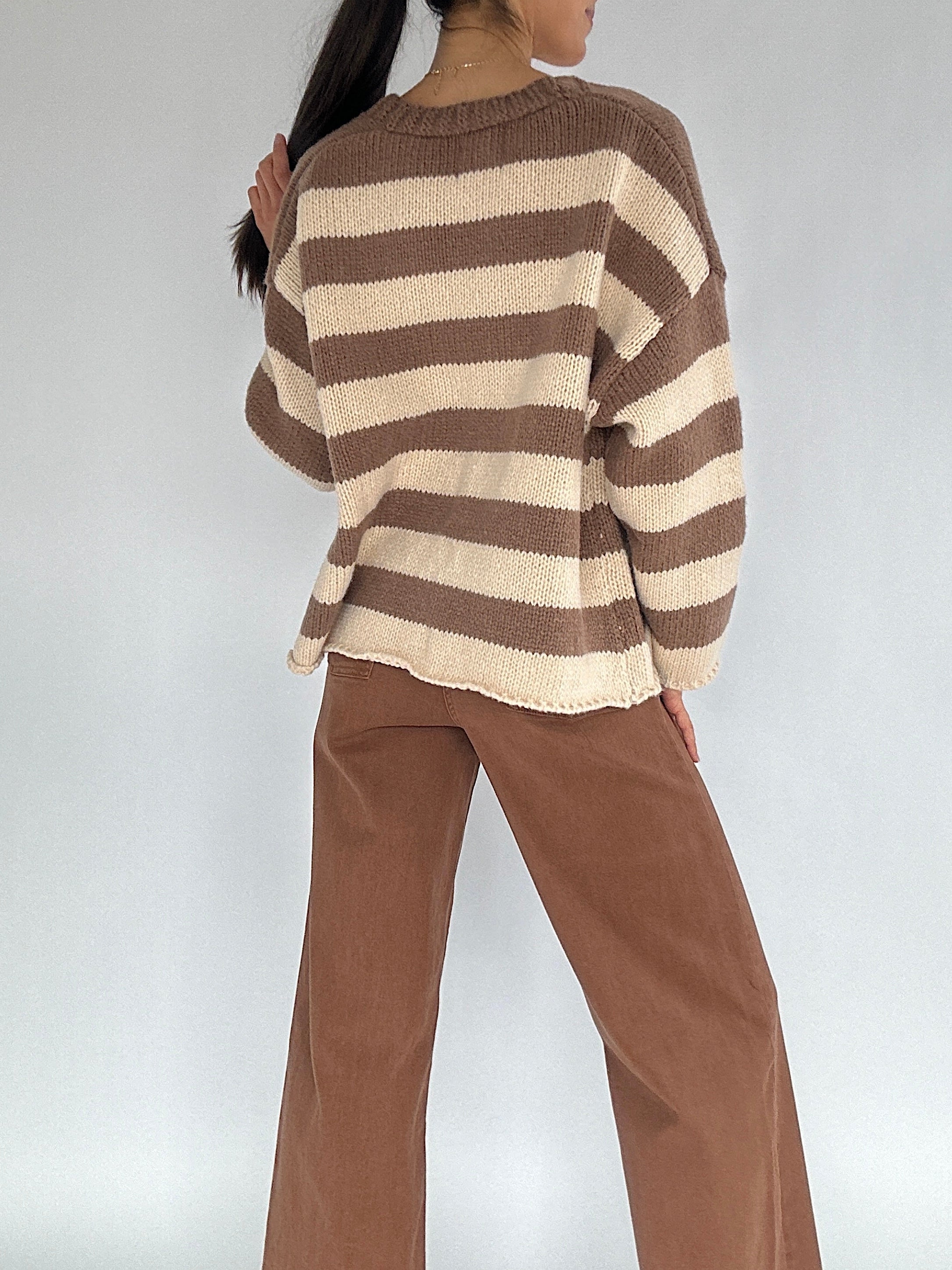 Person wearing a brown and beige striped sweater with brown pants on a white background from back