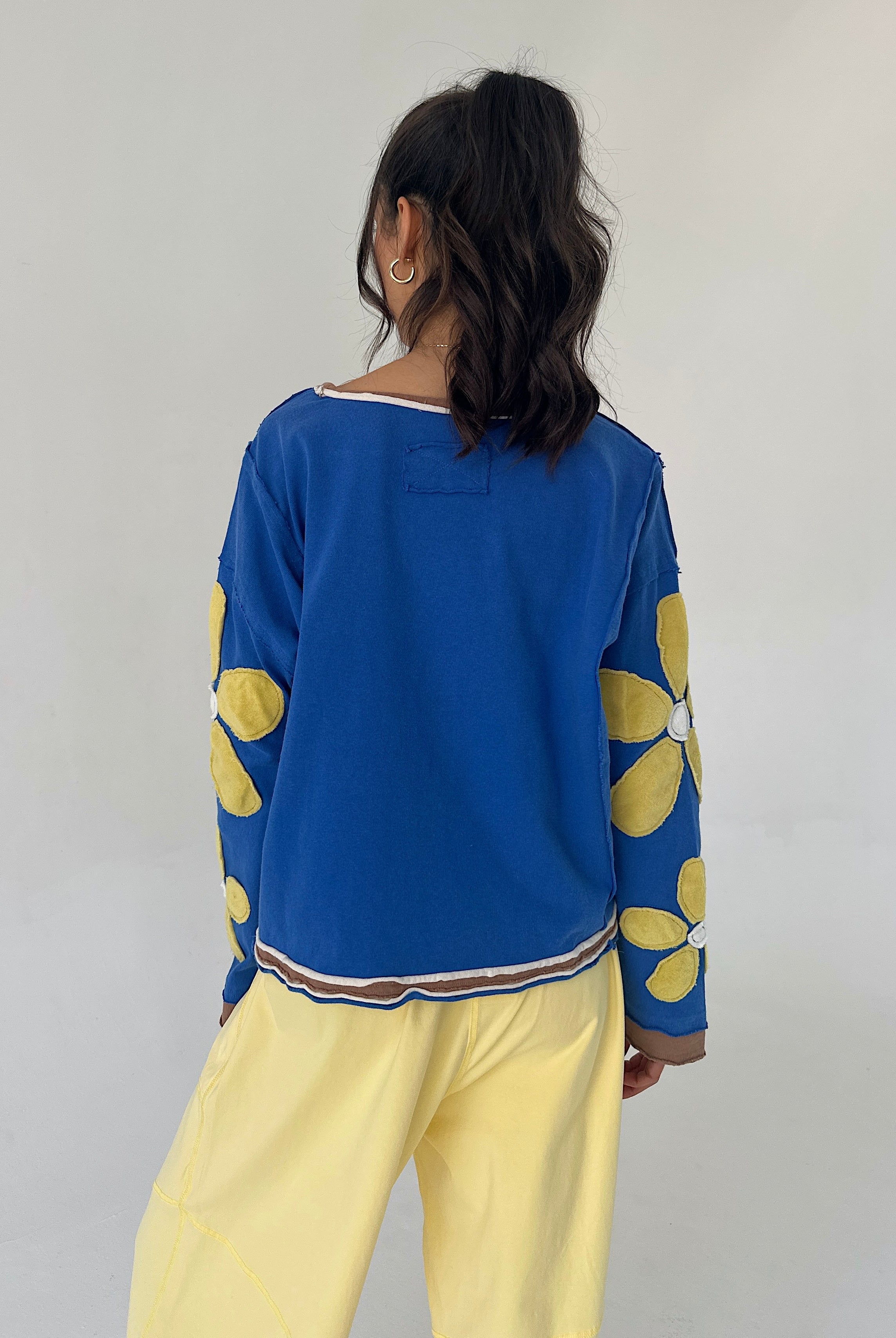 Person wearing a blue pullover with yellow floral patterns and yellow pants against a plain background