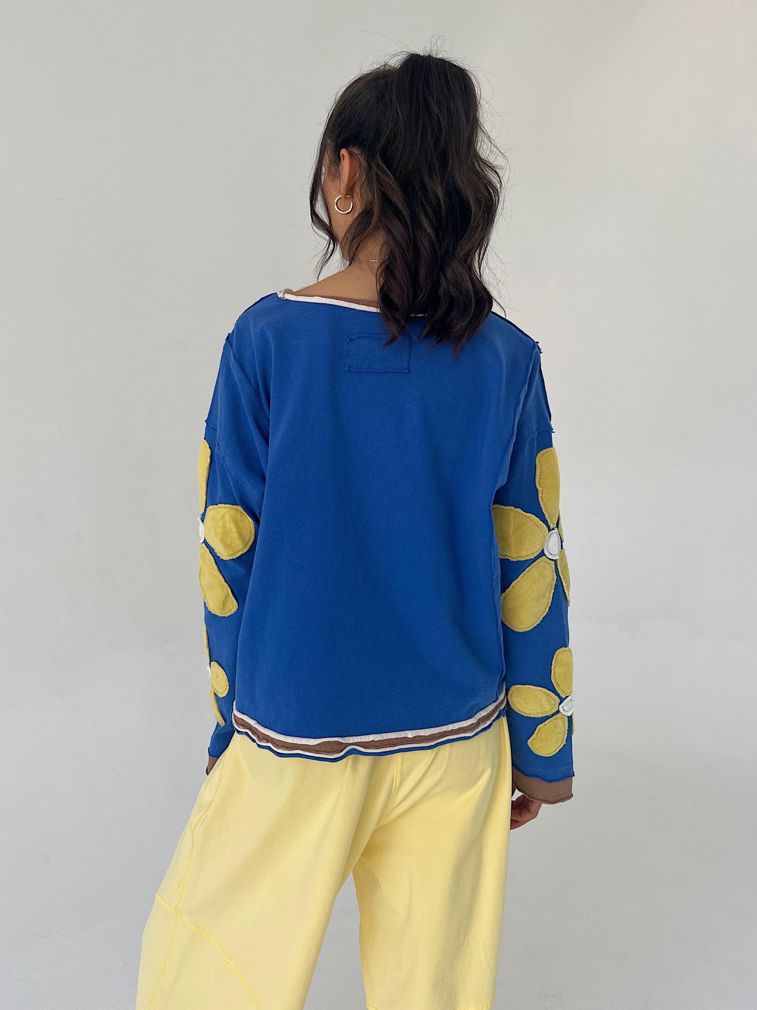 Person wearing a blue pullover with yellow floral patterns and yellow pants against a plain background