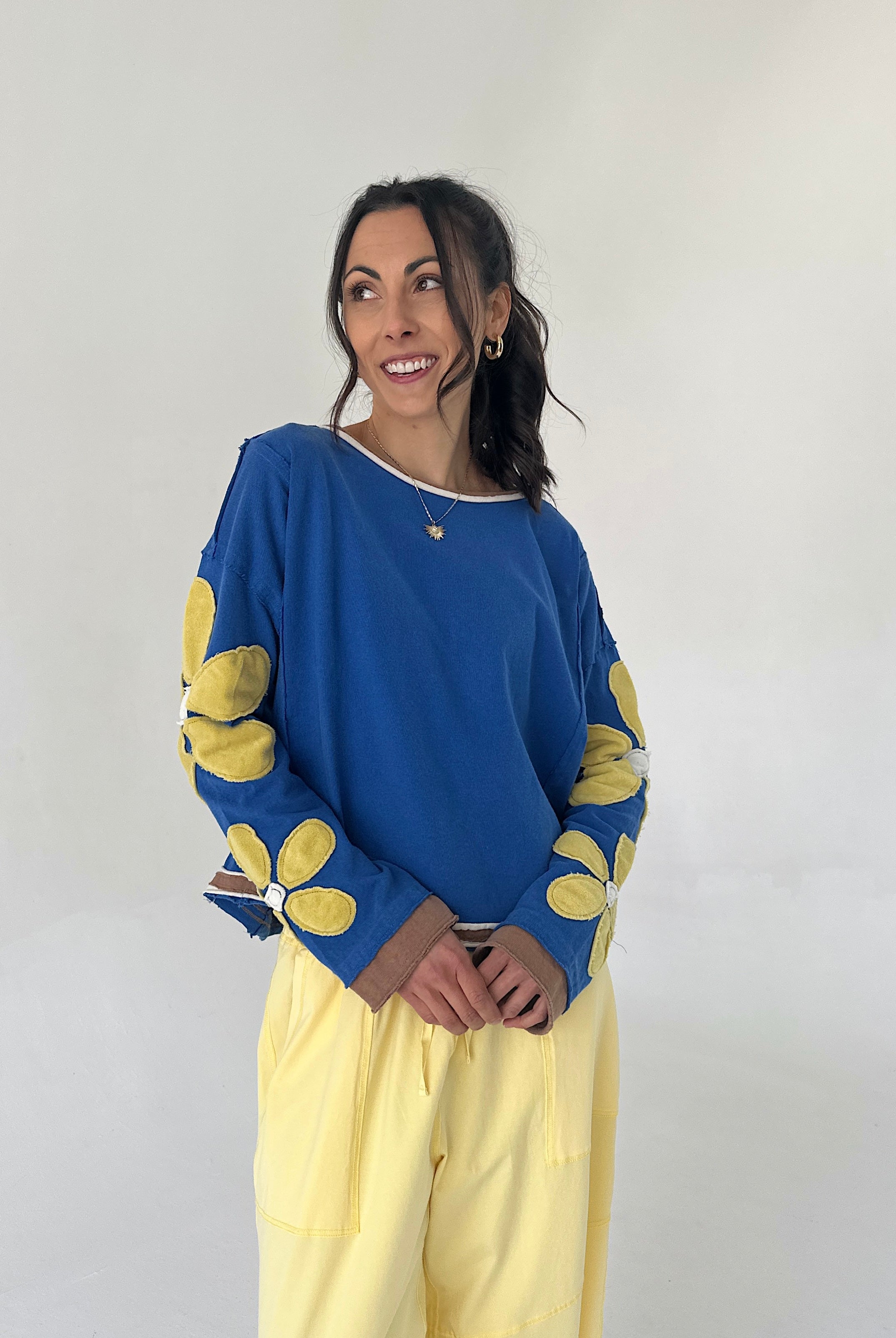 Woman wearing a blue sweater with yellow flower patterns and yellow pants against a white background