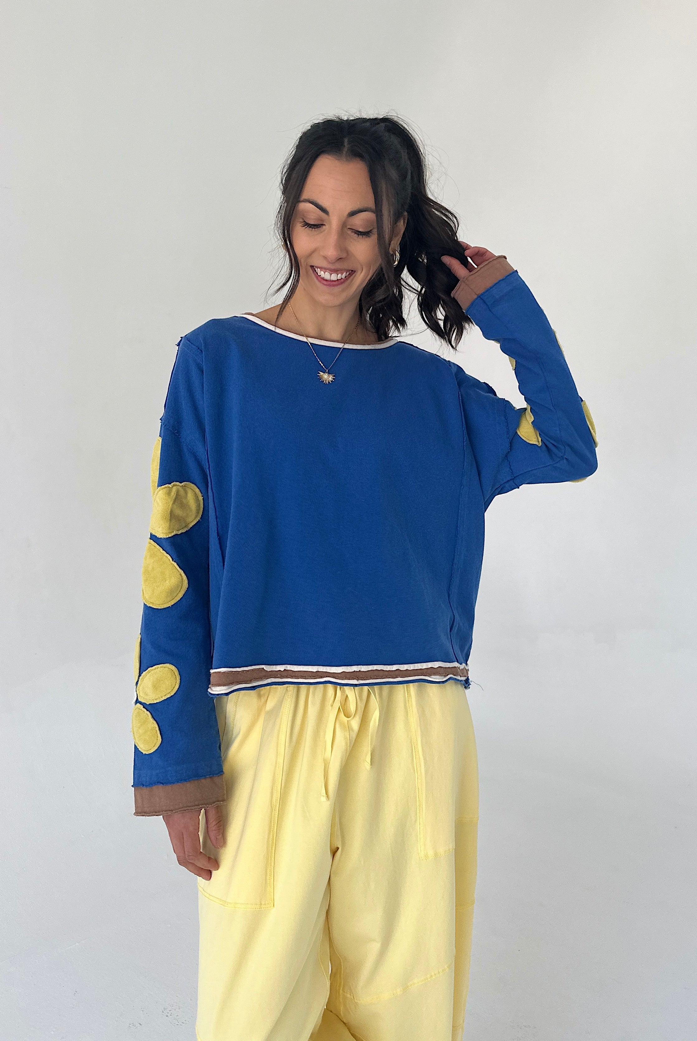 Woman wearing a blue sweater with yellow polka patches and yellow pants against a white background