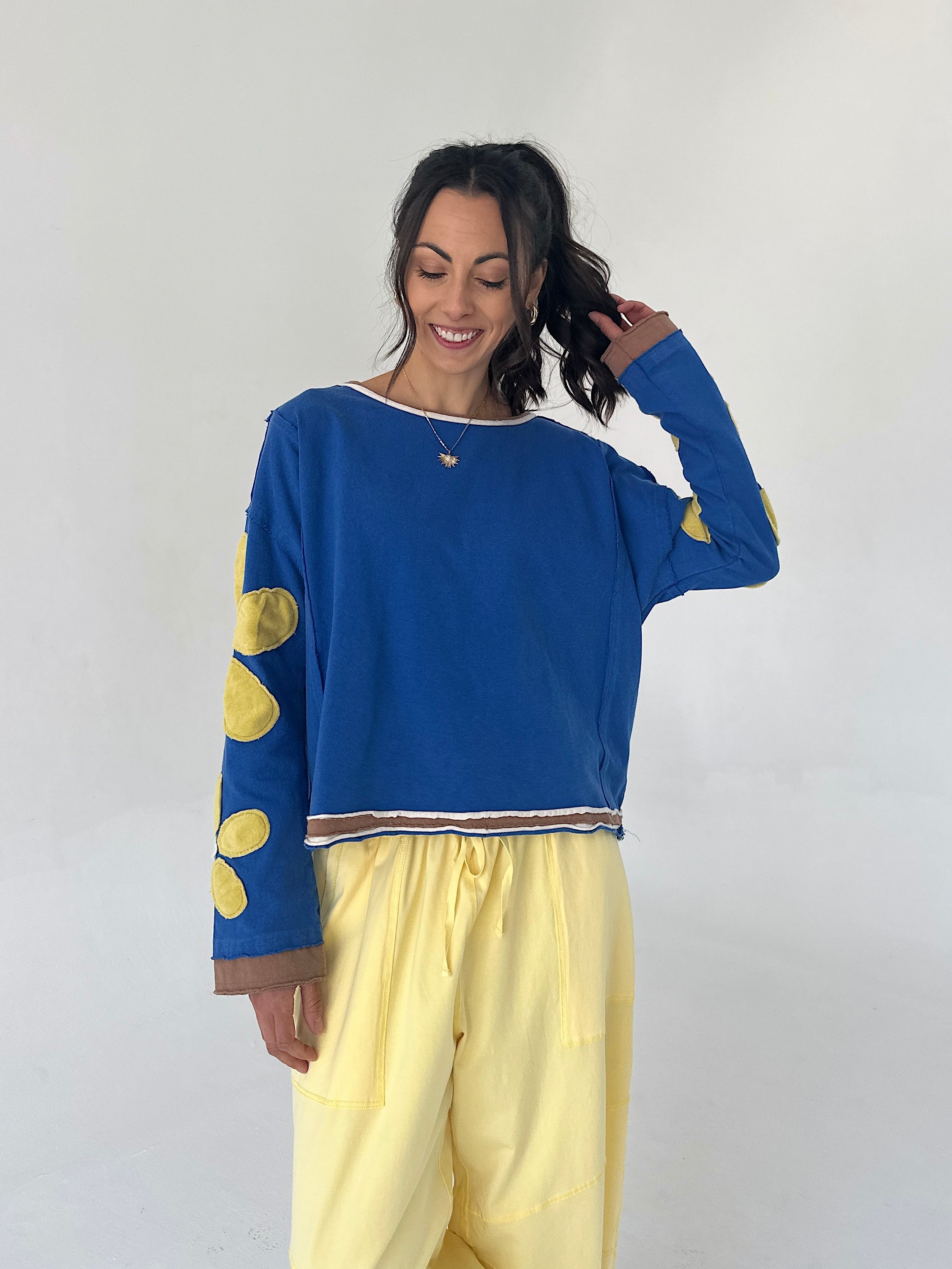 Woman wearing a blue sweater with yellow polka patches and yellow pants against a white background