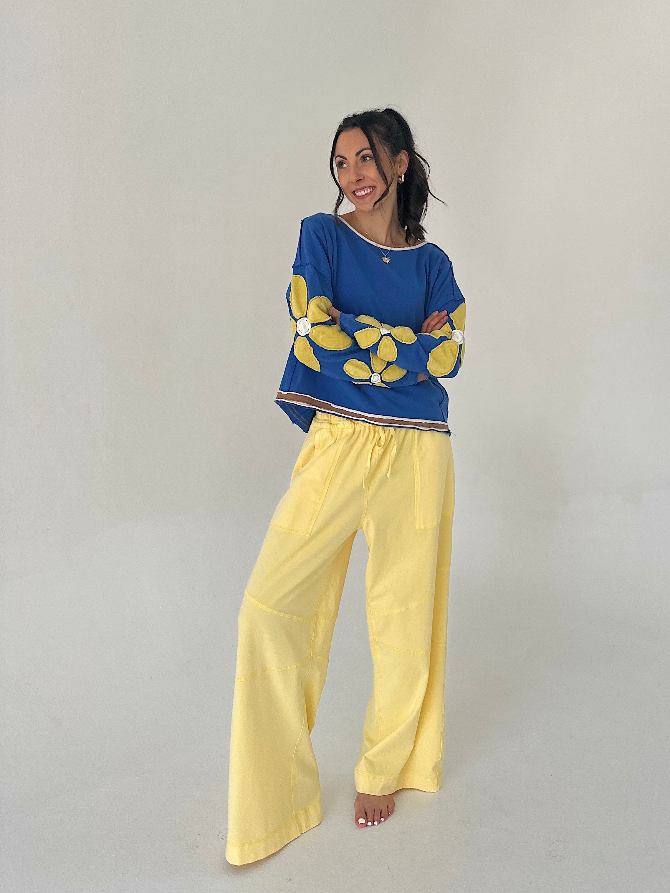 Woman wearing a blue sweater with yellow floral patterns and yellow pants on a plain background