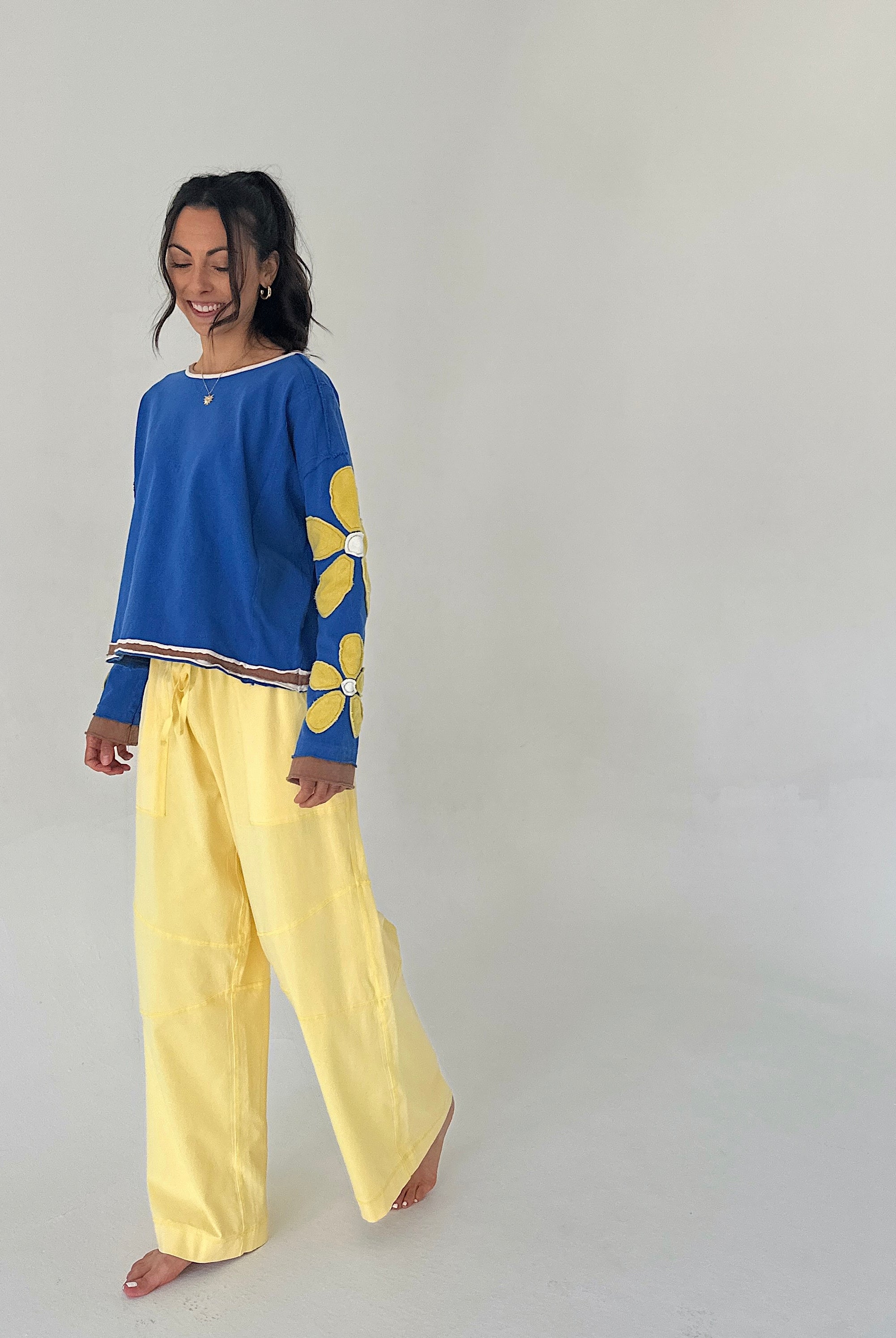 Woman wearing a blue top with floral designs and yellow pants on a plain background