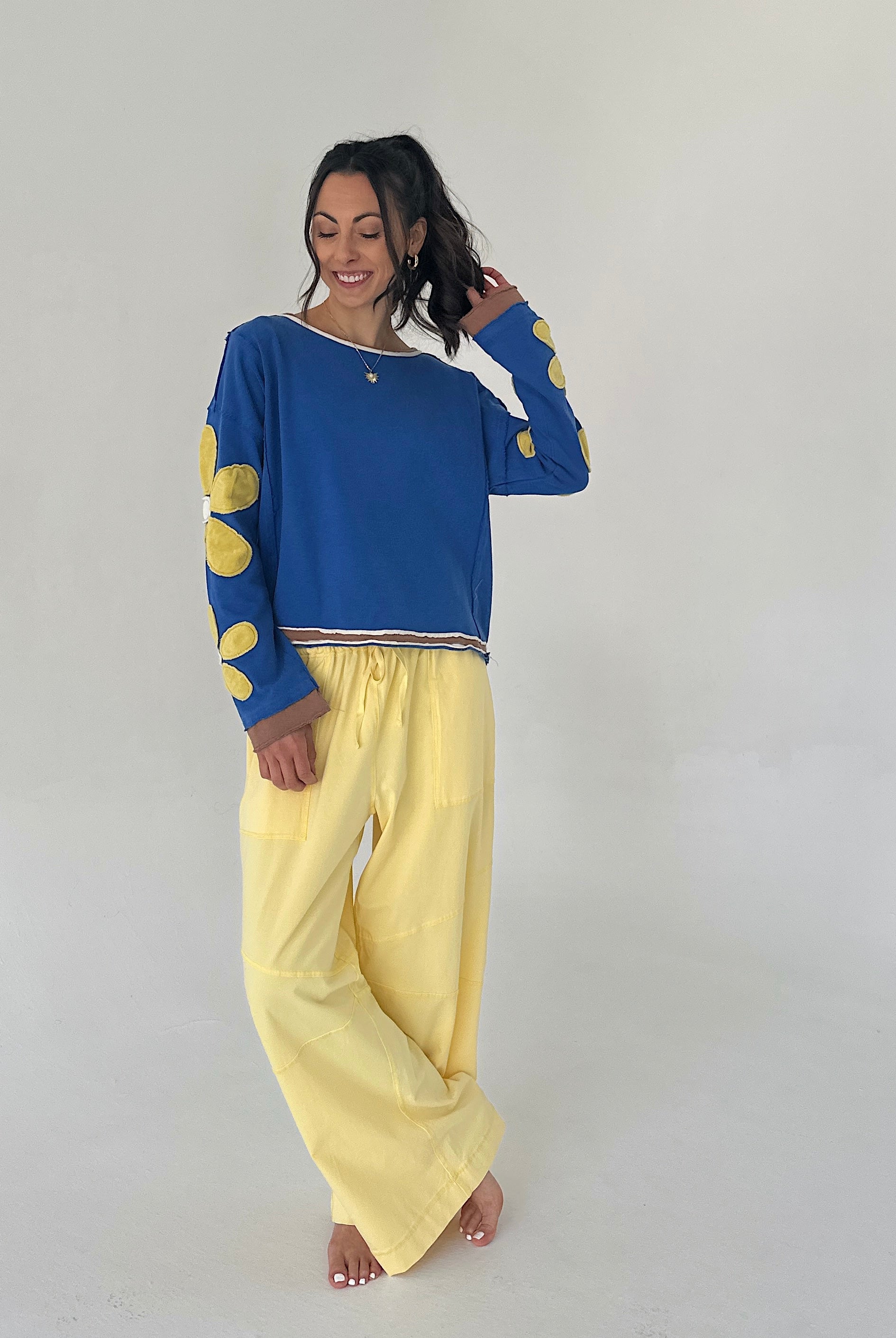 Woman wearing a blue top with yellow patterns and yellow pants on a plain background