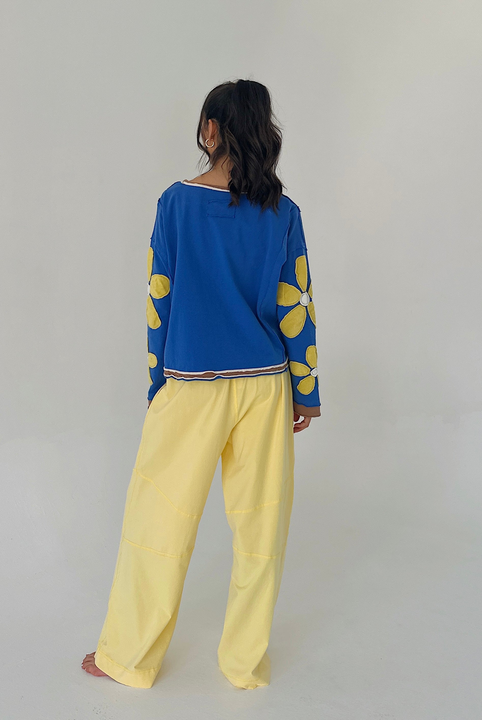 Person wearing a blue top with yellow floral patterns and yellow pants on a plain background